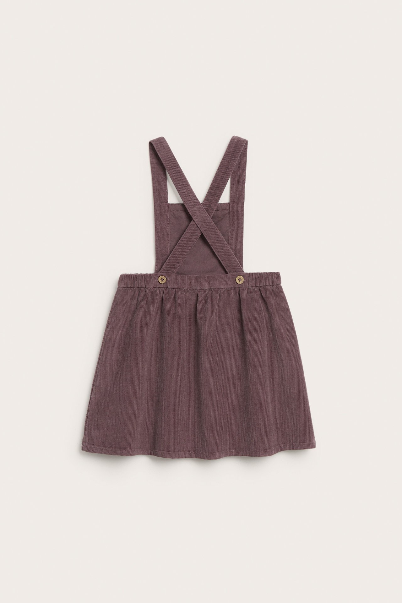Rückansicht eines lila Kinder-Cord-Latzkleides mit elastischem Bund und gekreuzten Knopfriemen.