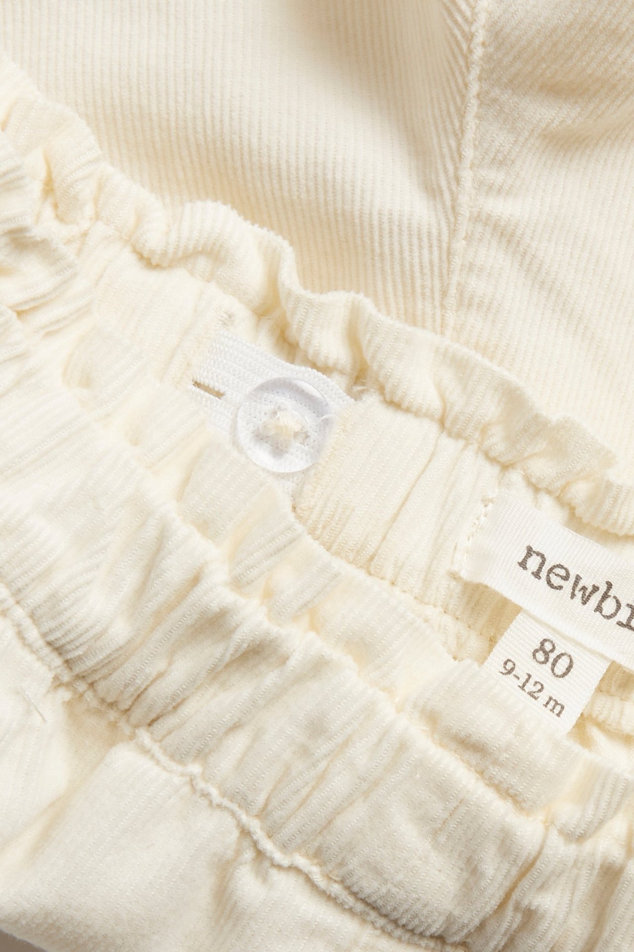 Nahaufnahme von hellbeiger Cordhose mit elastischem Bund und verstellbarem Knopf.