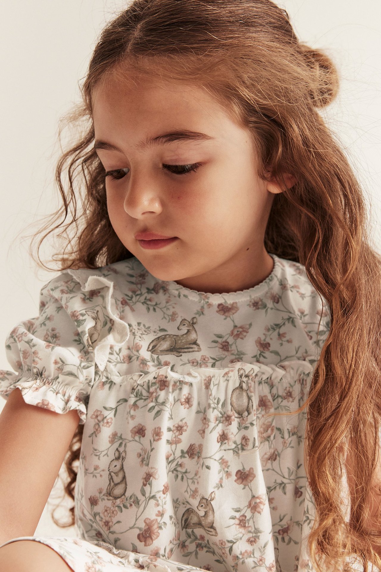 Close-up of a kid in an off-white floral and animal print cotton jersey dress with puff sleeves.