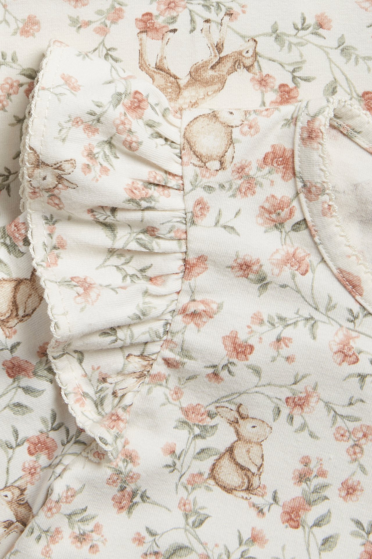 Close-up of an off-white baby top with ruffles, featuring a delicate floral and bunny print.