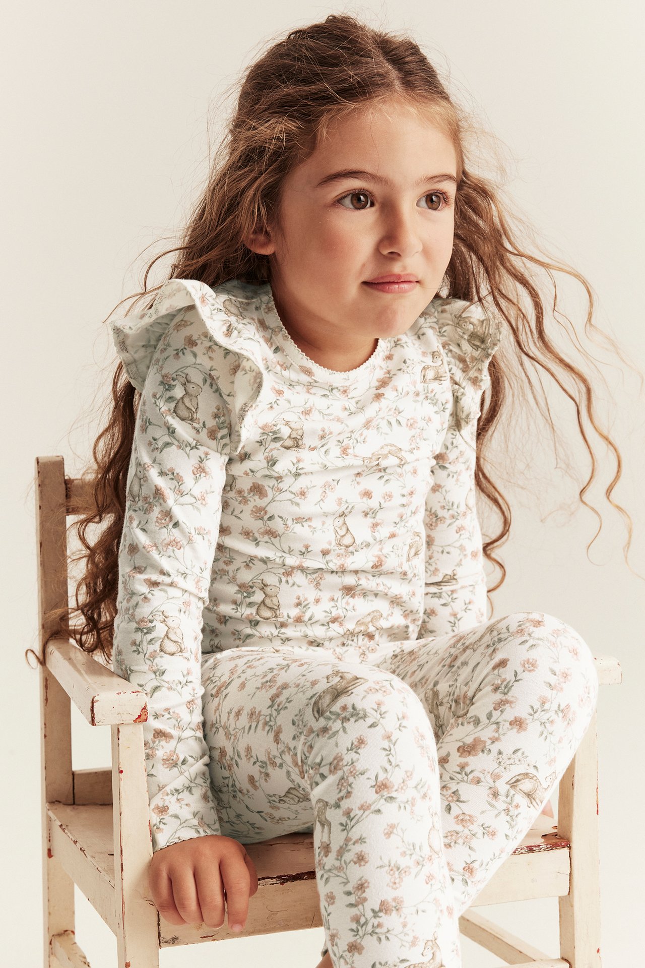 Front view: Kid in off-white floral bunny print long-sleeved top with ruffles and matching leggings.