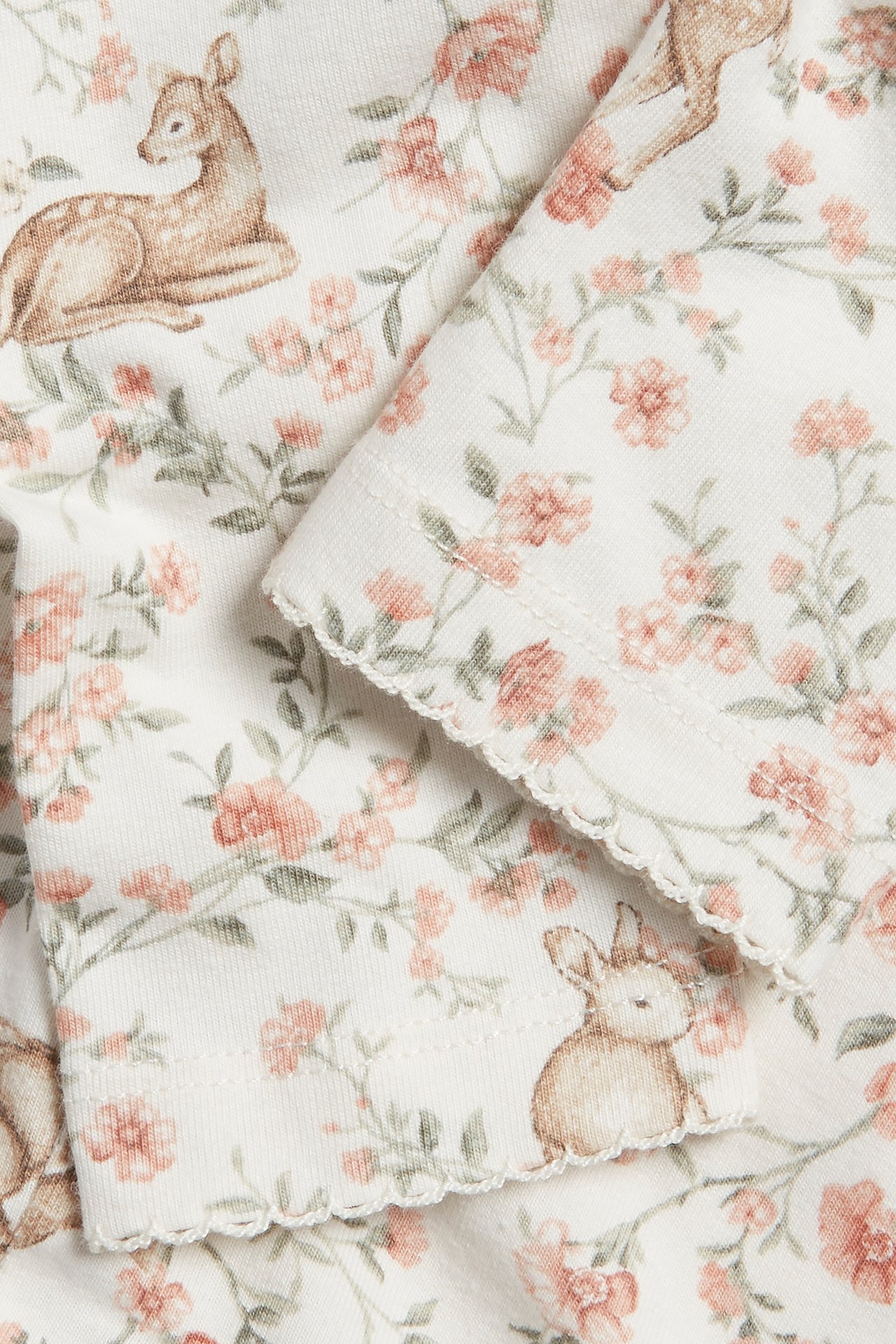 Close-up of off-white cotton blend leggings with floral, deer, and rabbit pattern, picot hem.