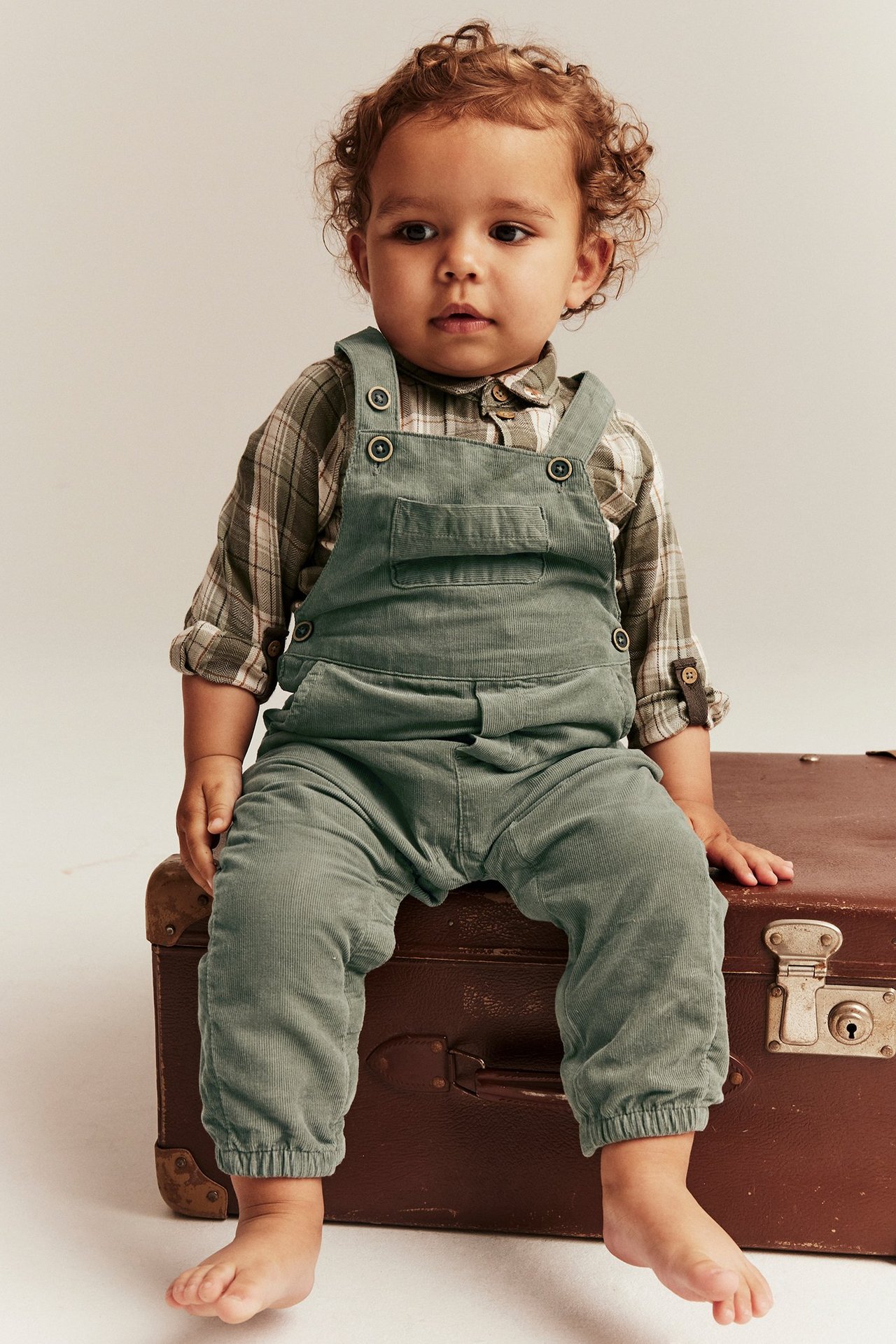 Kind in dunkelgrünen Manchester-Hängseln mit Knöpfen, Taschen, Gummizug, Frontalansicht.