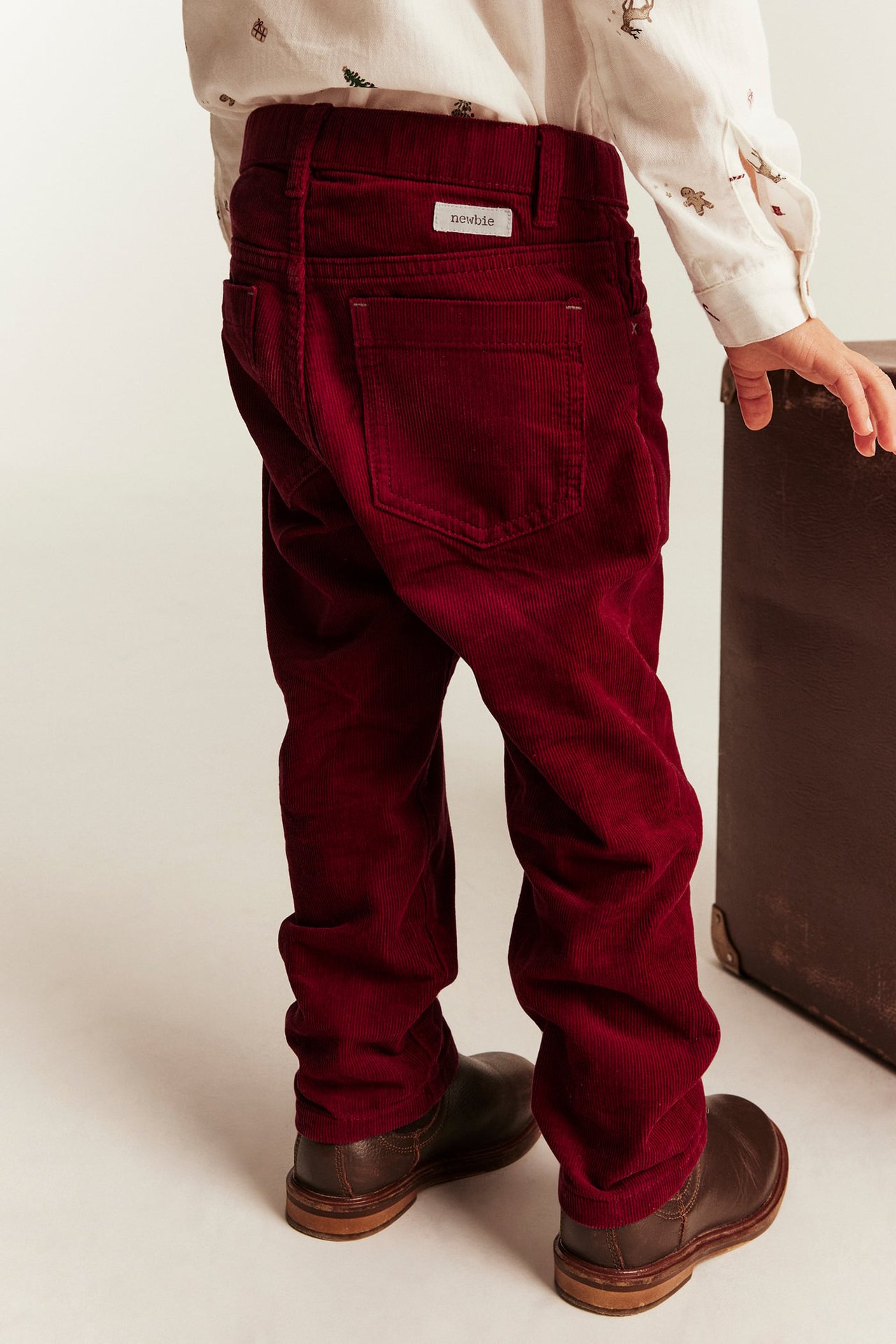 Back view of a kid in red corduroy pants, a white patterned shirt, and brown boots.