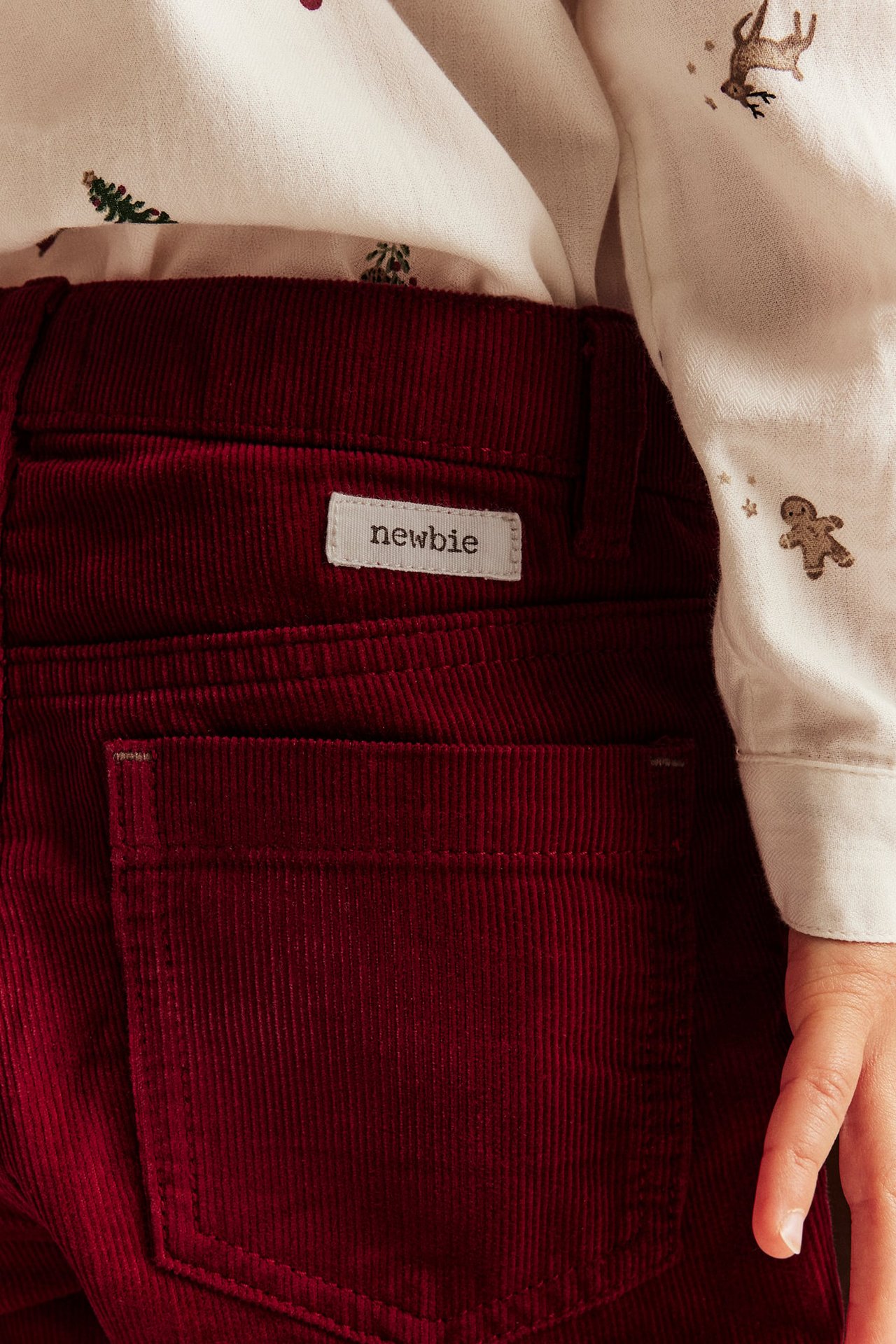 Close-up of kid's burgundy corduroy pants with white label on back pocket, with cream embroidered shirt.