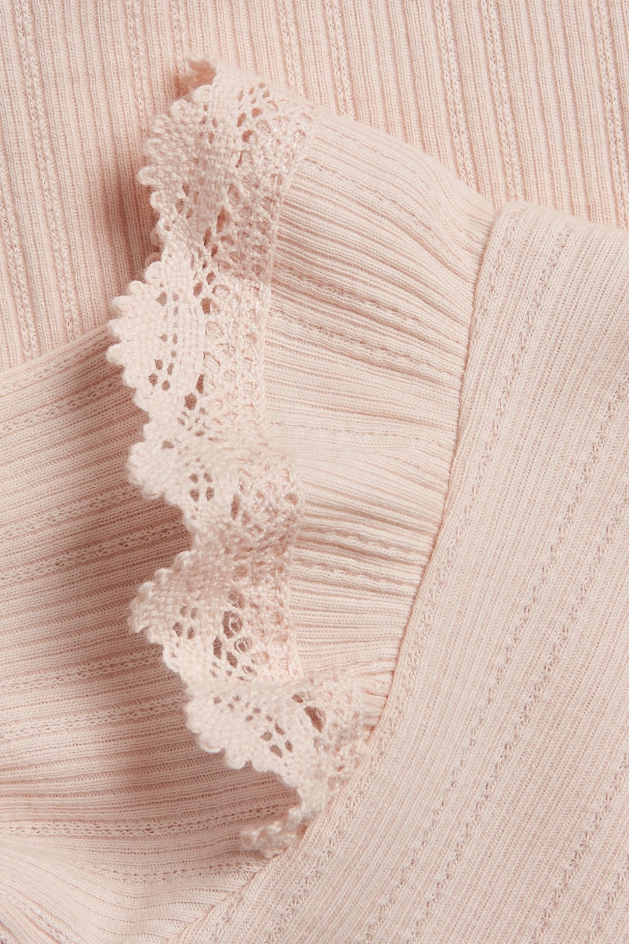 Close-up of a light pink ribbed baby bodysuit with a delicate lace-edged ruffle on the shoulder.