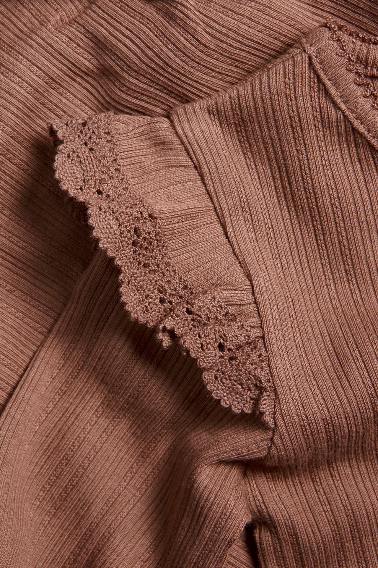 Nahaufnahme eines dunkelrosa gerippten Baby-Bodys mit Rüschen und Spitzenbesatz an der Schulter.