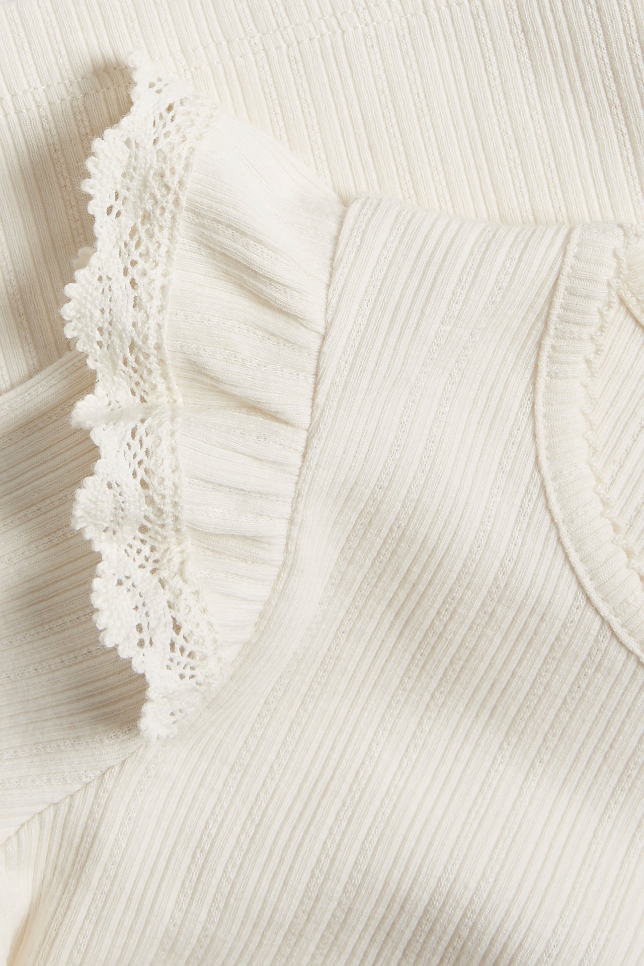 Close-up of an off-white ribbed top with ruffles and lace trim on the shoulder.