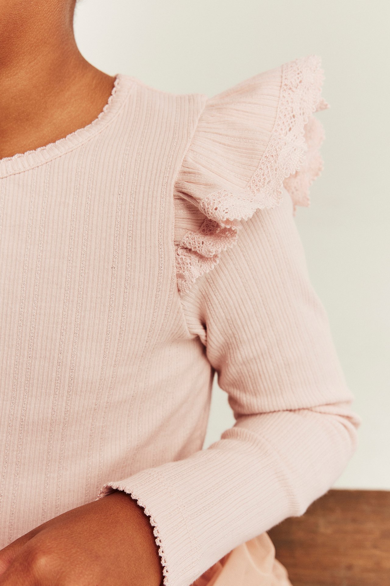 Kid's light pink ribbed long-sleeve top with ruffle lace trim and scalloped edges.