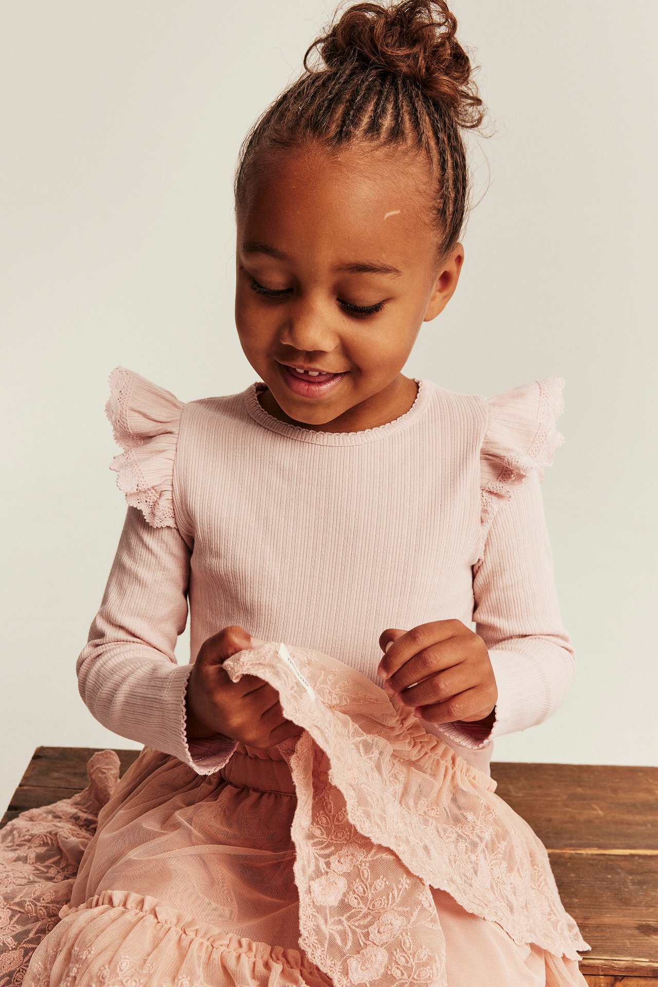 Front view of kid wearing pink ribbed long-sleeved top with ruffles, holding pink lace tulle skirt.