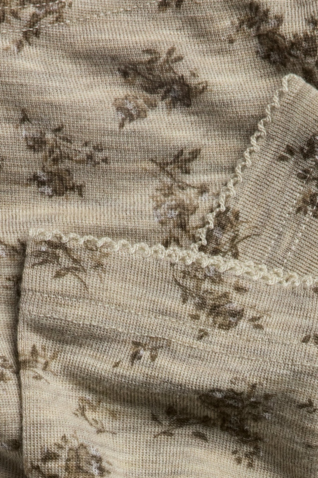 Close-up of beige melange knitted merino wool leggings with brown floral print and picot trim.
