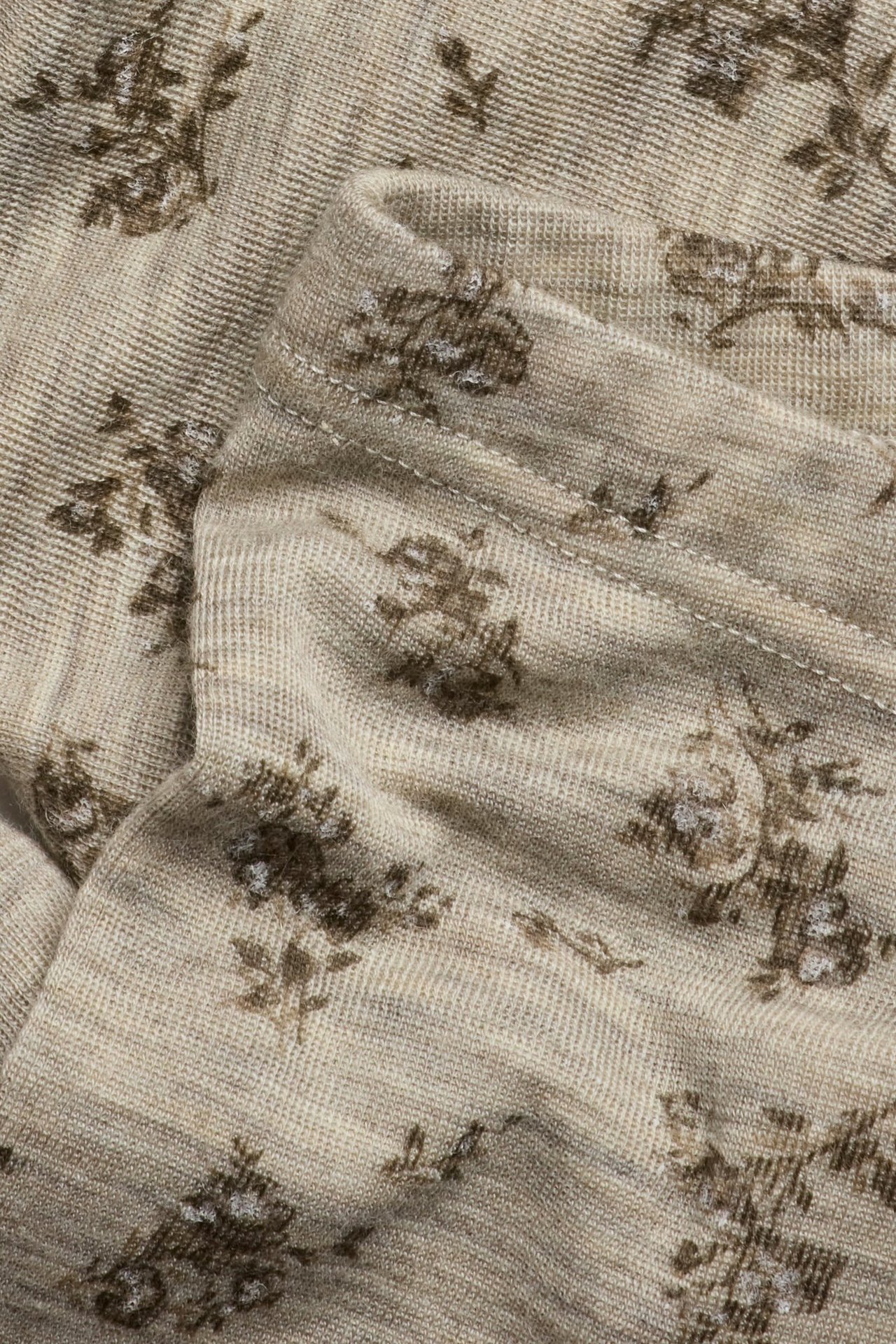 Close-up of beige melange knitted merino wool leggings with a brown floral print and visible seam.