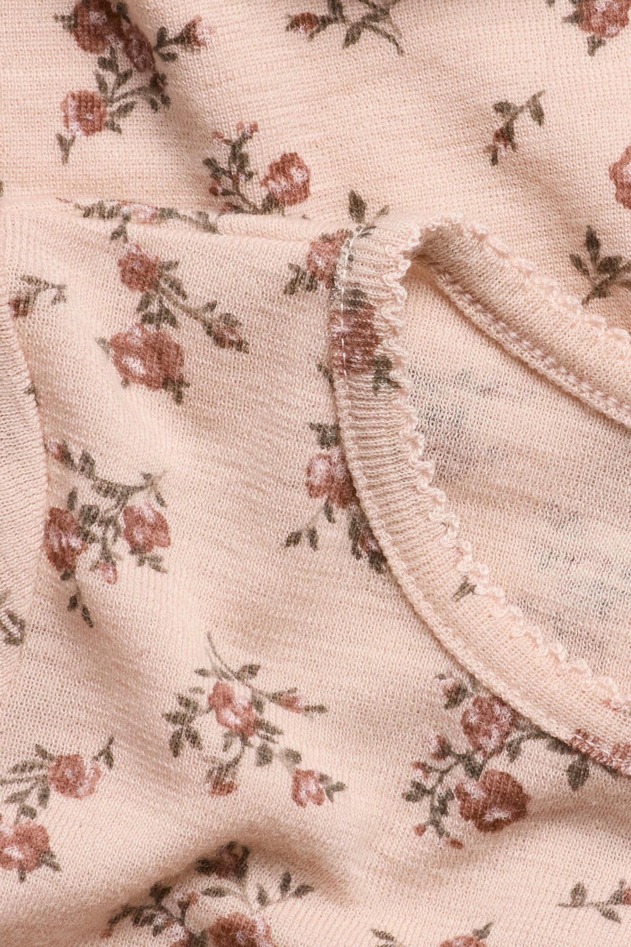 Nahaufnahme eines rosa gestrickten Merinowoll-Tops mit Blumenmuster und Picot-Stich am Halsausschnitt.