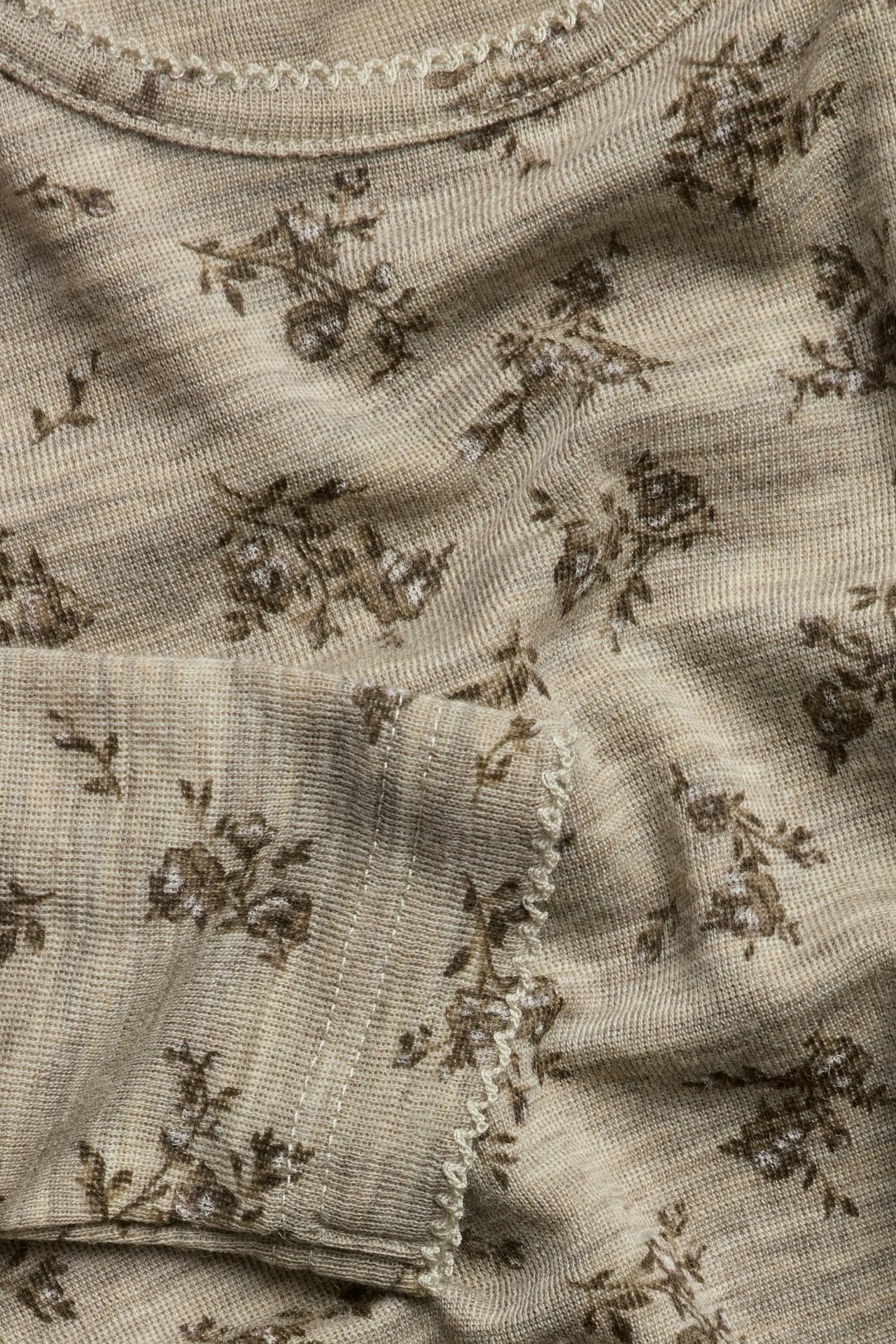Nahaufnahme eines beigefarbenen melierten Stricktops aus Merinowolle mit braunem Blumenmuster und Picot-Besatz.