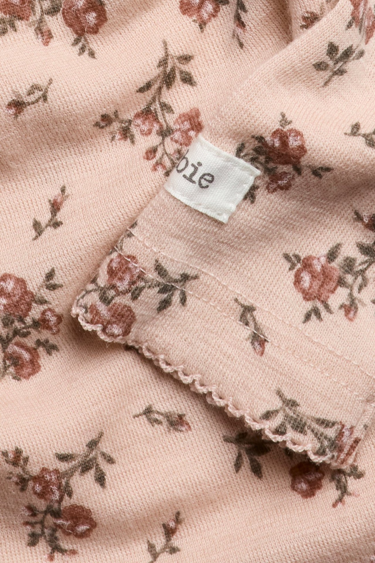 Nahaufnahme eines rosa gestrickten Baby-Bodys aus Merinowolle mit Blumenmuster und Picot-Borte.