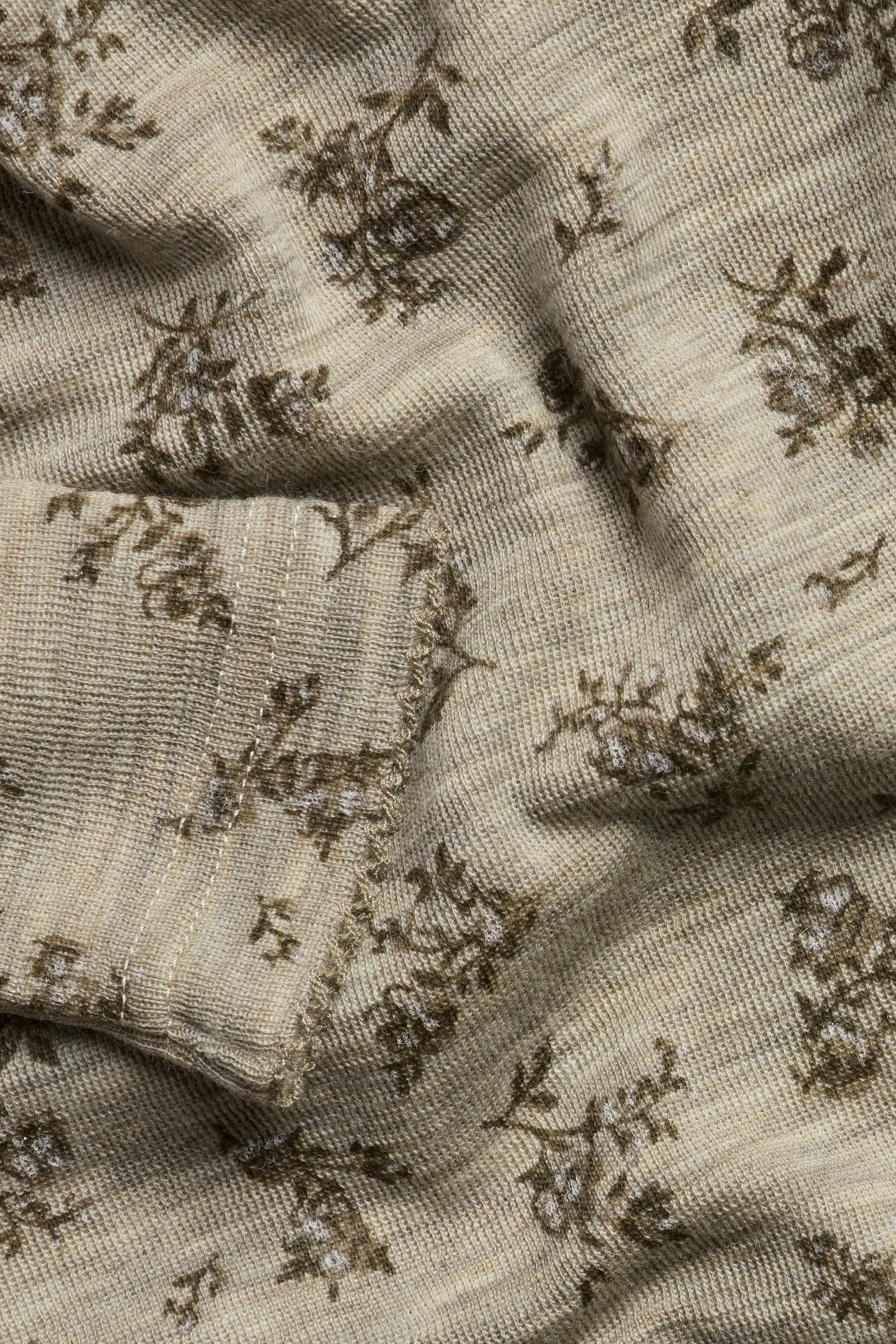 Close-up of a beige melange knitted merino wool bodysuit fabric with a brown floral pattern.