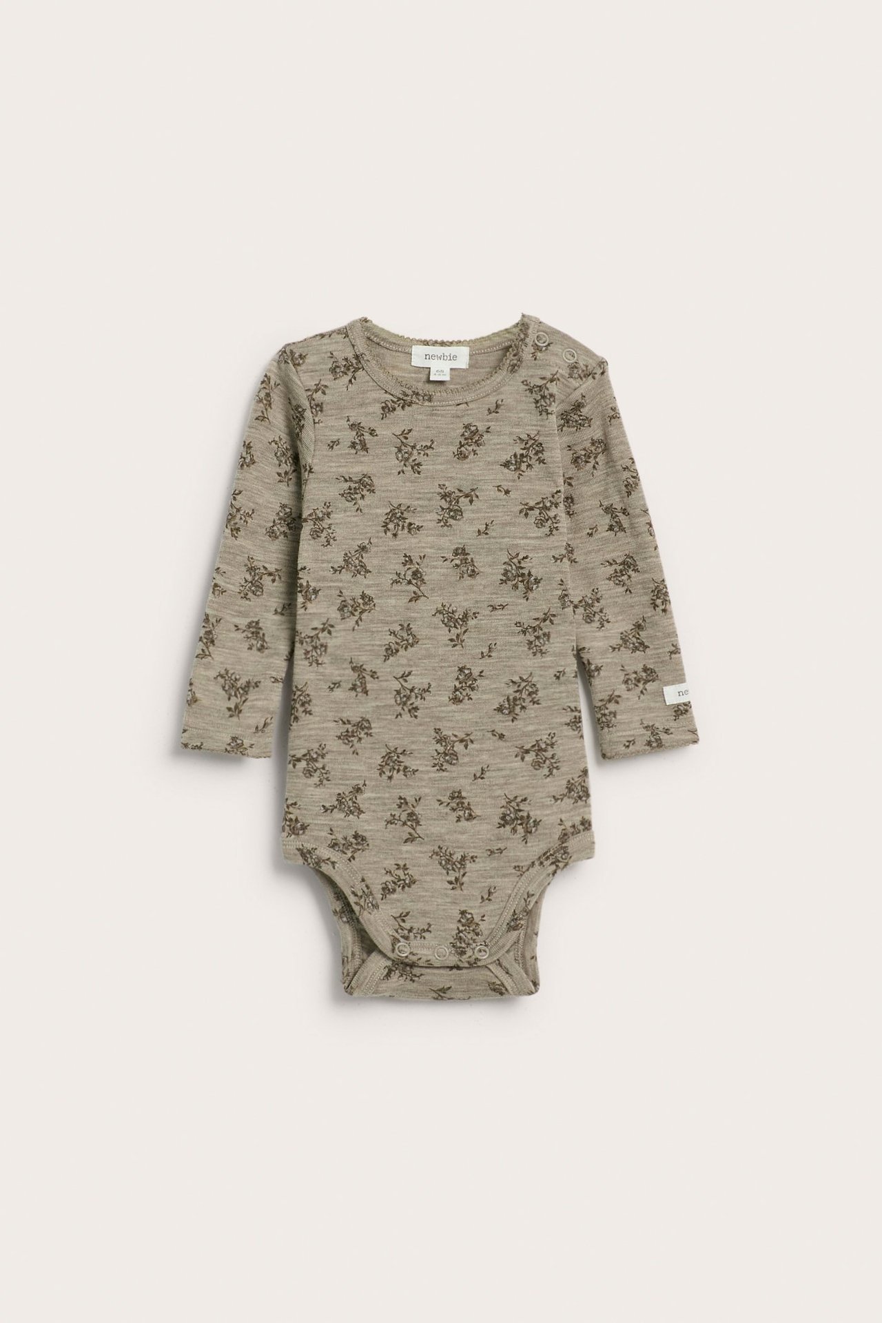 Front view of a beige melange knitted merino wool baby bodysuit with a dark floral print and snap buttons.