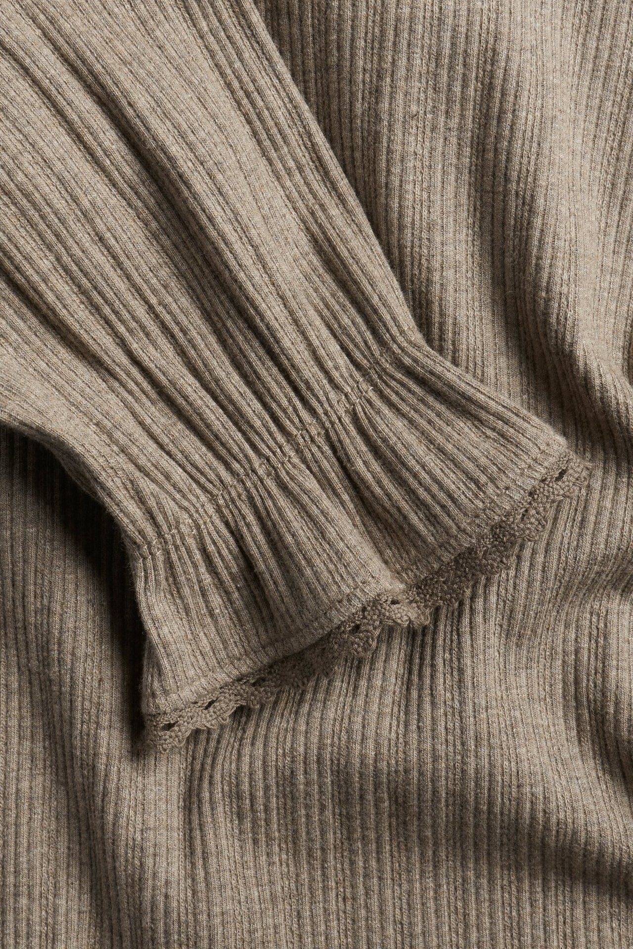 Nahaufnahme eines braunmelierten Rippen-Tops mit Rüschenärmelbündchen und zarter Spitzenkante.