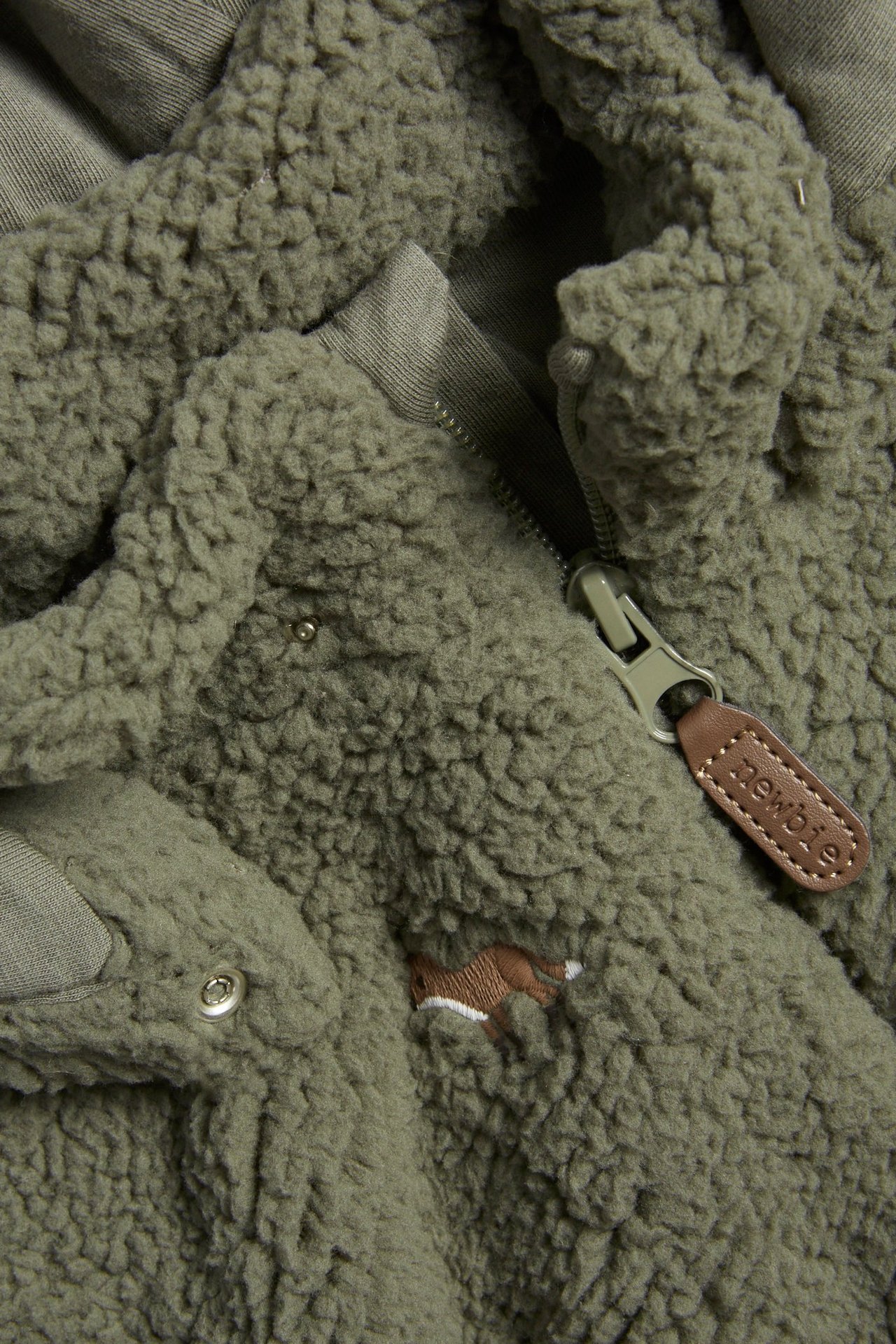 Nahaufnahme einer dunkelgrünen Pile-Jacke mit gesticktem Fuchs, Reißverschluss und Druckknopf.