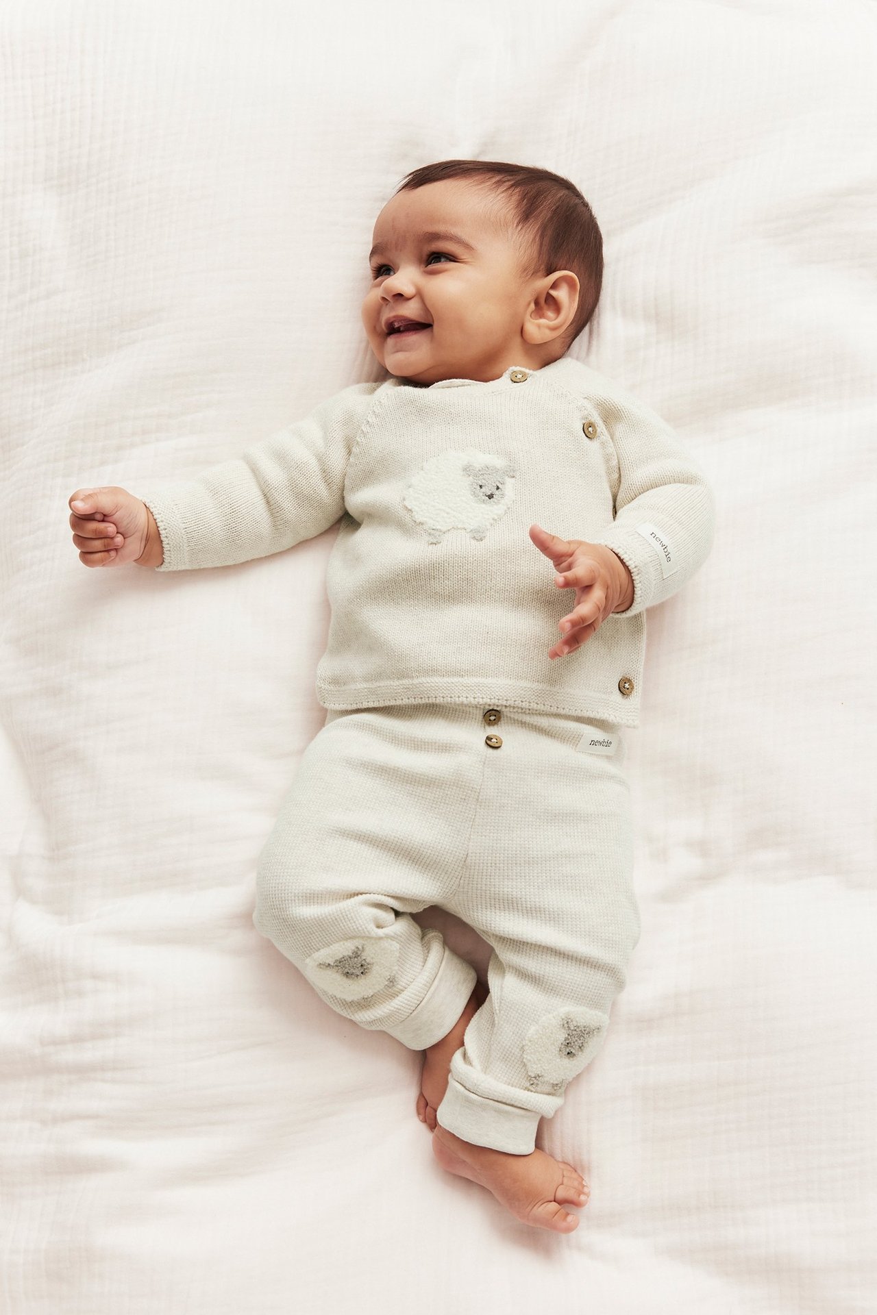 Draufsicht eines Babys in beiger Melange Strick-Wickeljacke mit Schaf und passender Hose.