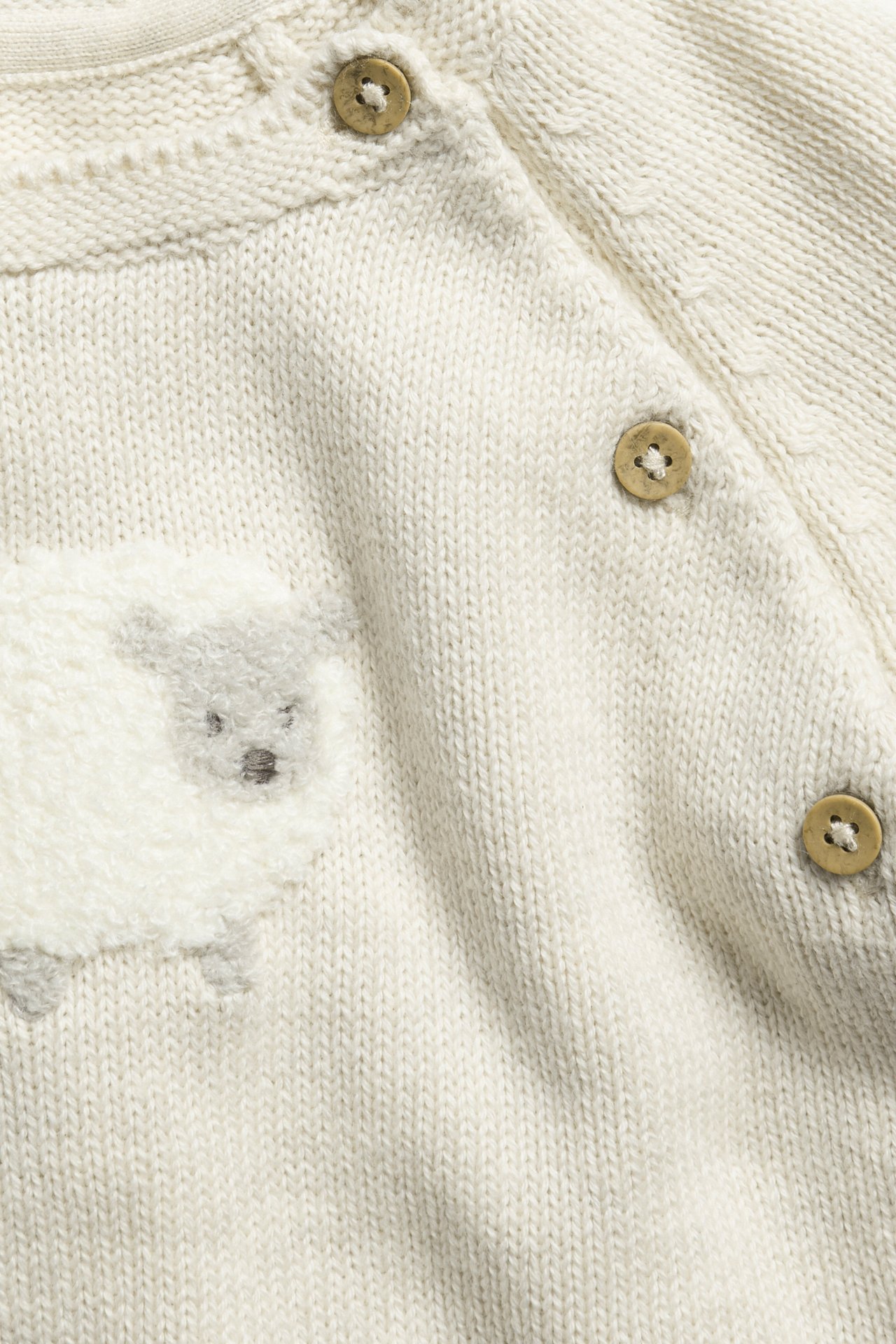 Close-up of a beige melange knitted cotton wrap cardigan with a sheep application and three brown buttons.