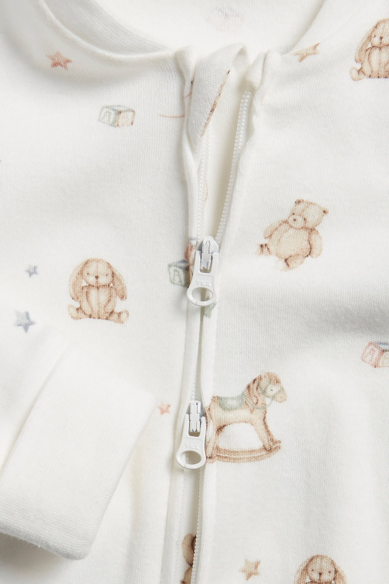 Close-up of an off-white baby romper with a toy pattern and a two-way zipper.