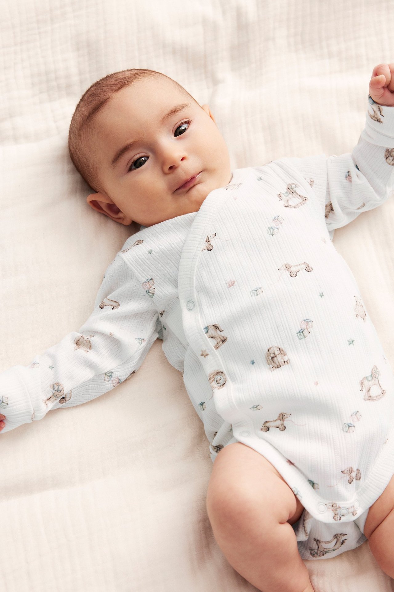 Top-down view: Baby in off-white ribbed wrap bodysuit with colorful toy pattern and snap buttons.