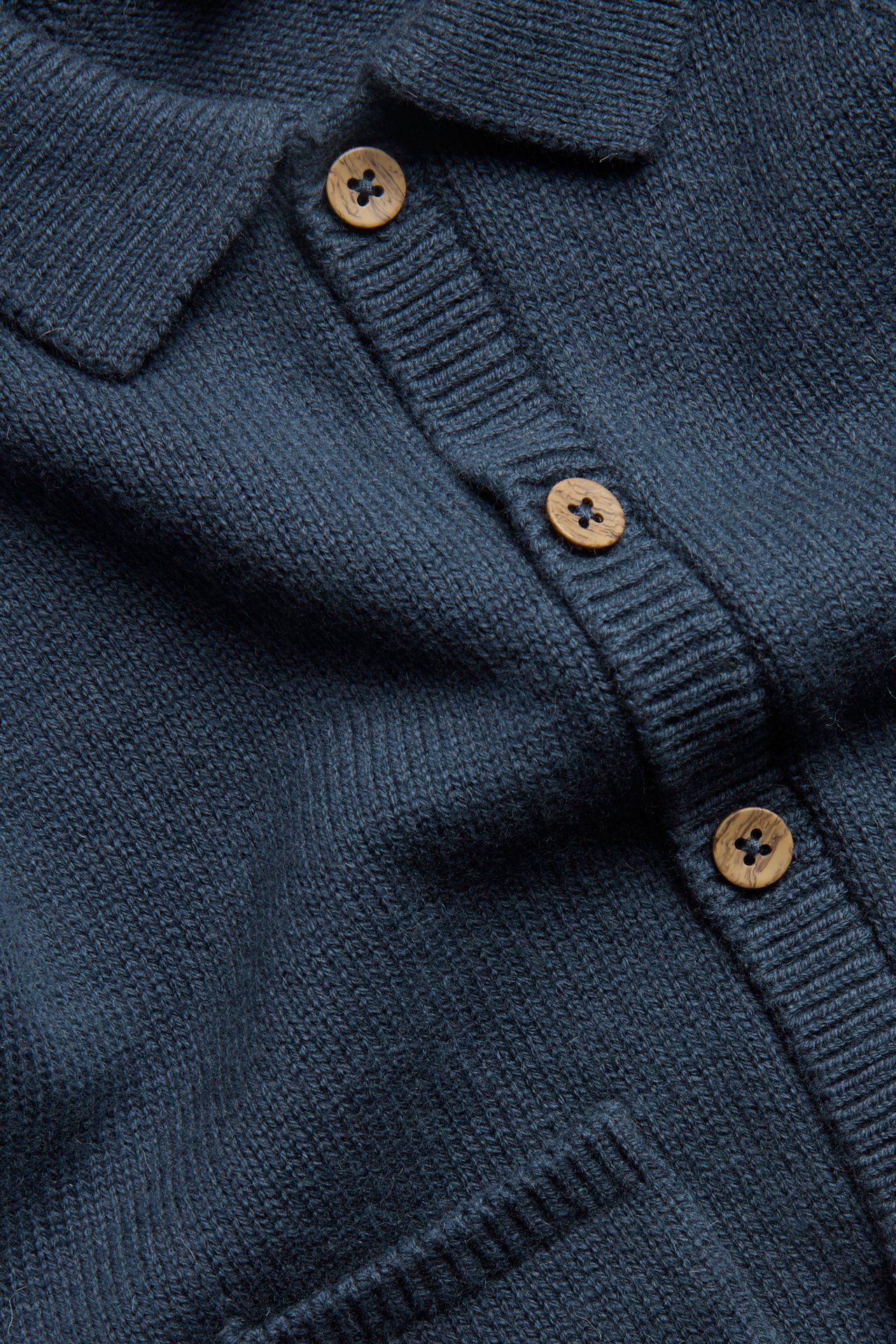 Nahaufnahme einer dunkelblauen Strickjacke aus Wollmischung mit Kragen, Knopfleiste und Holzknöpfen.