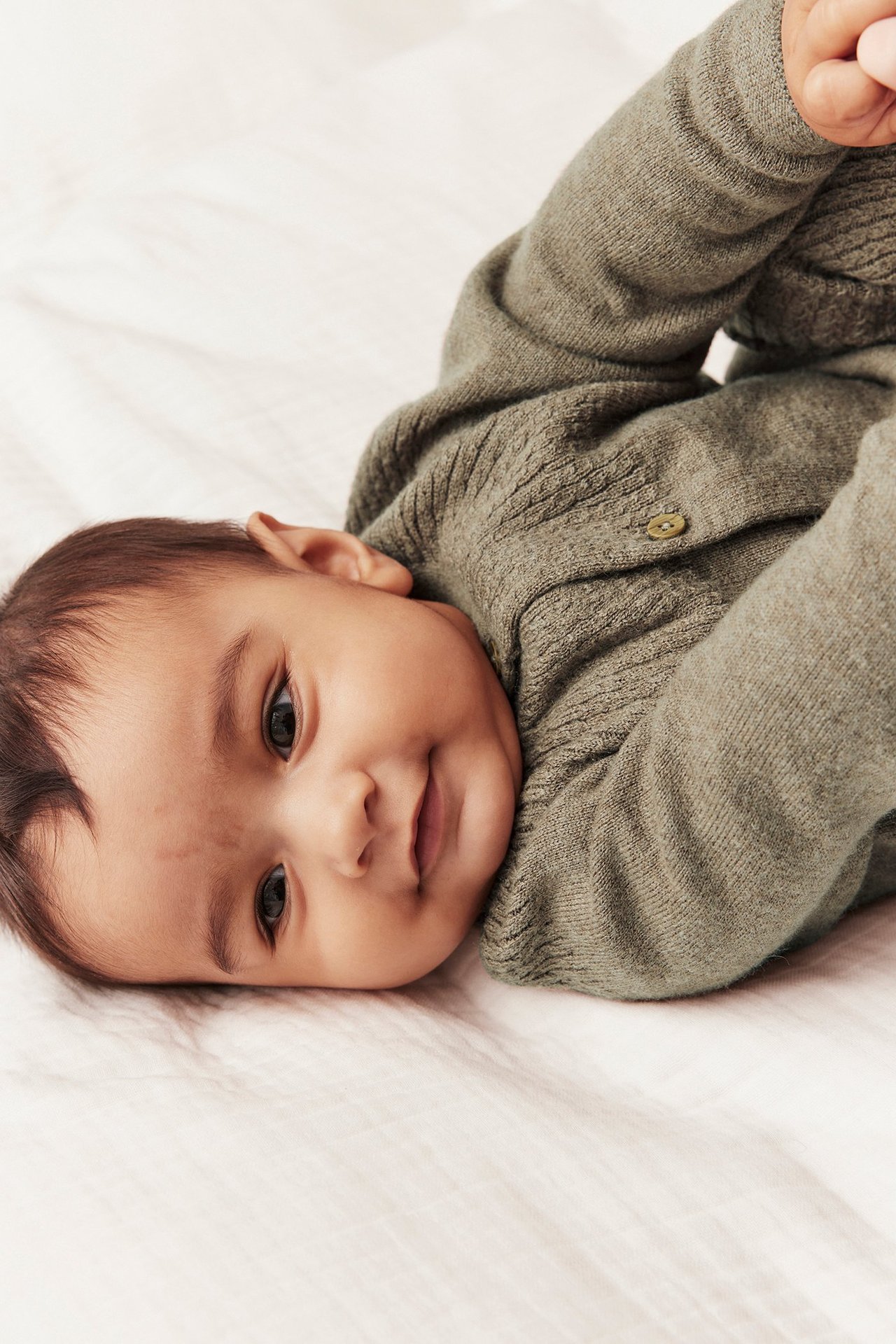 Close-up of a baby wearing a brown melange knitted wool-cotton cardigan with cable knit details and a button.