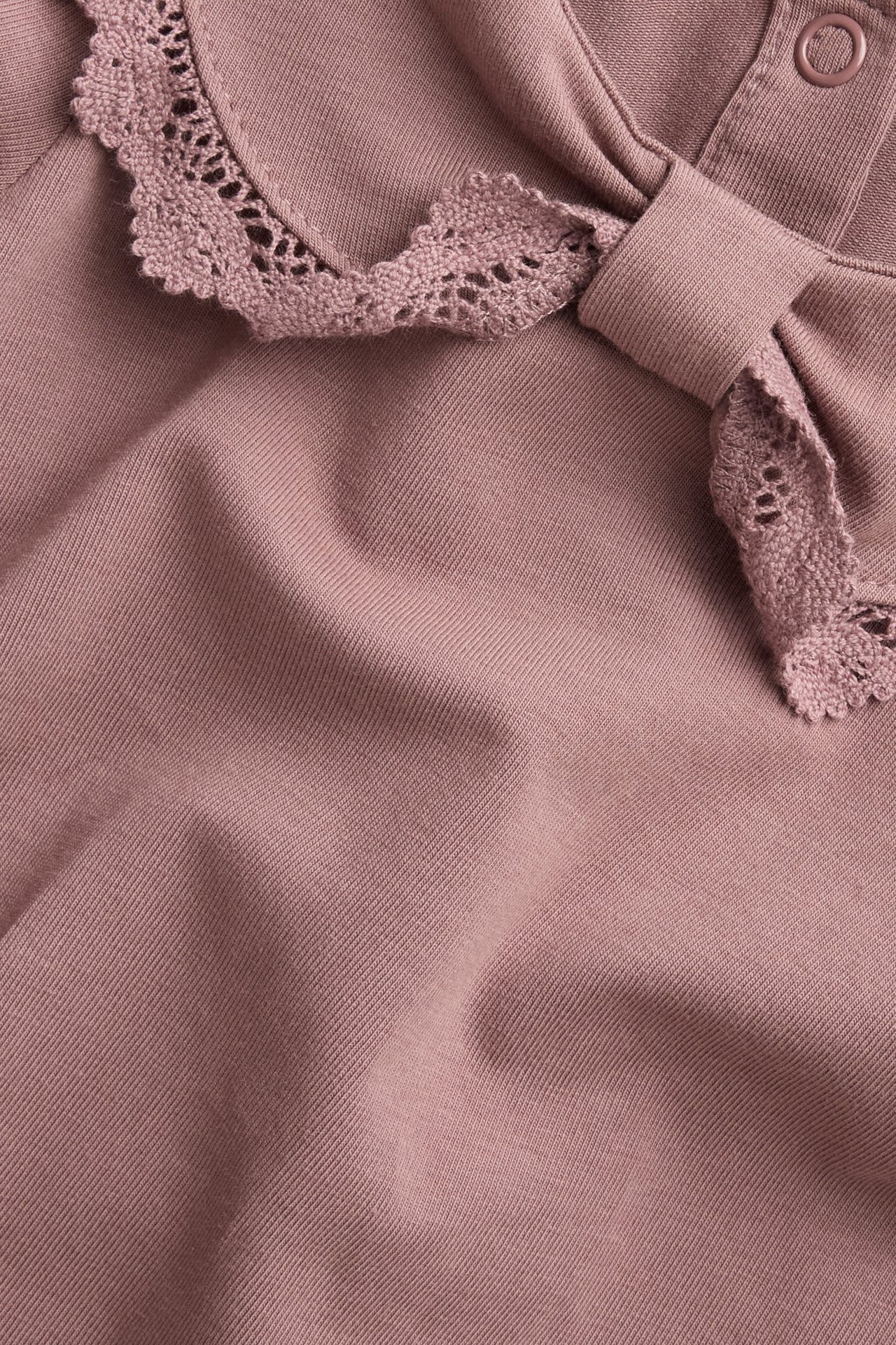 Nahaufnahme eines dunkelrosa Baby-Bodys mit spitzenbesetztem Schleifenkragen und sichtbarem Druckknopf.