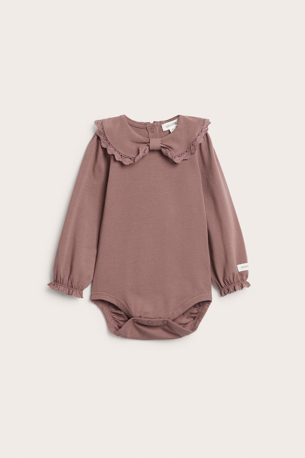Vorderansicht eines dunkelrosa Baby-Bodys mit Spitzenkragen, Schleife und Rüschenbündchen, Druckknöpfe.