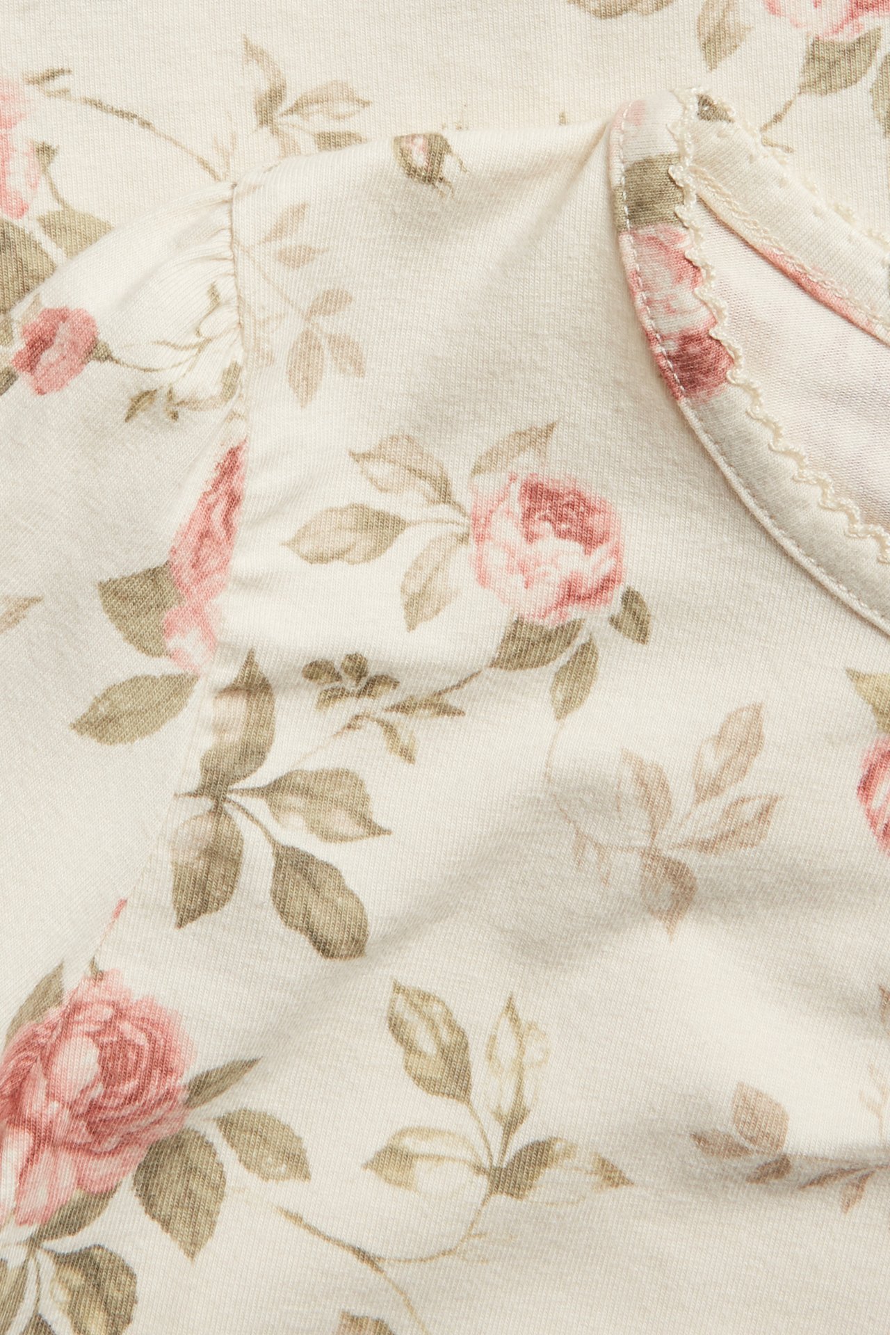 Close-up of a light beige top with pink floral print, puff sleeves, and picot trim at the neckline.
