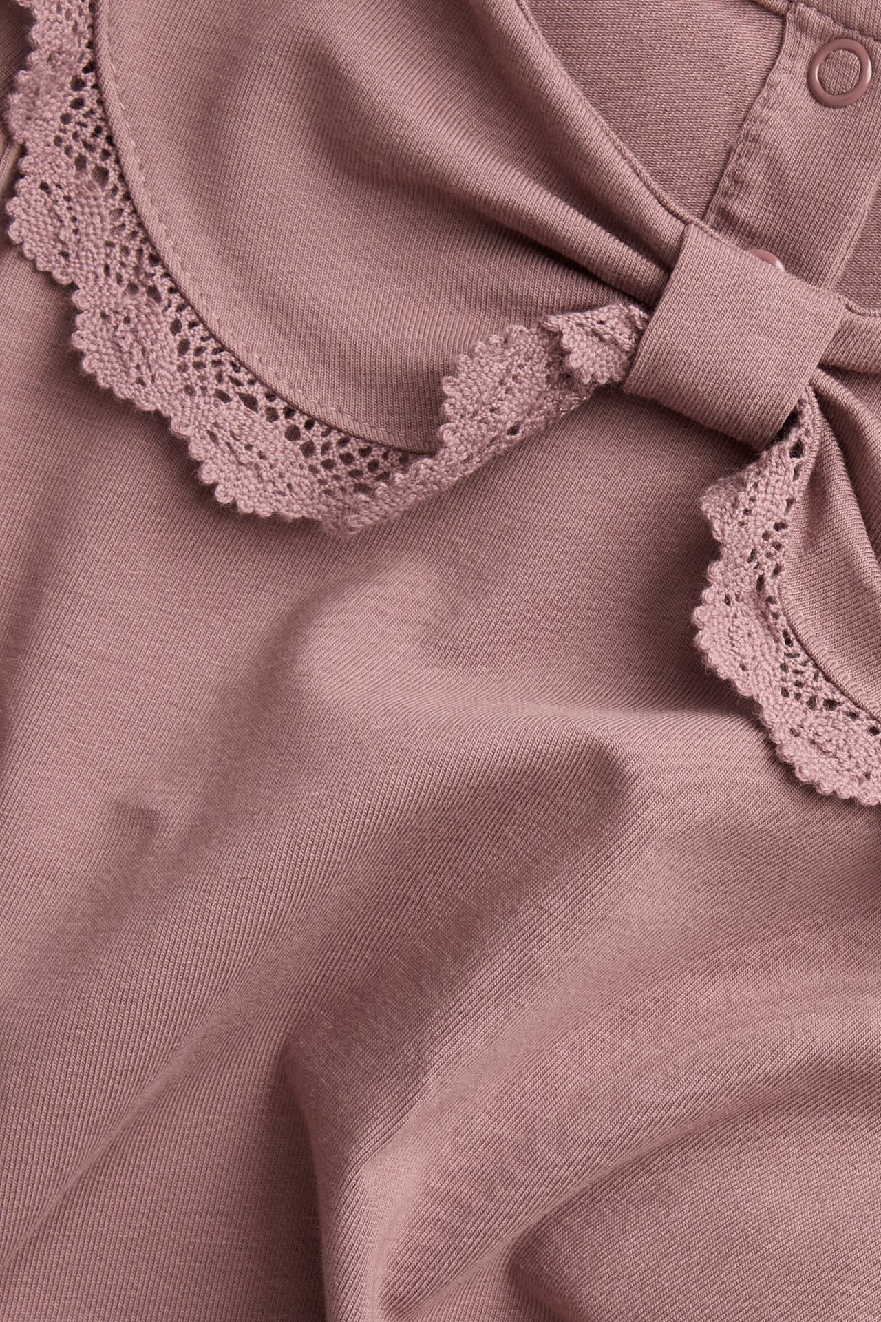 Close-up of a dark pink baby top with a lace-edged bow collar and snap buttons at the back.