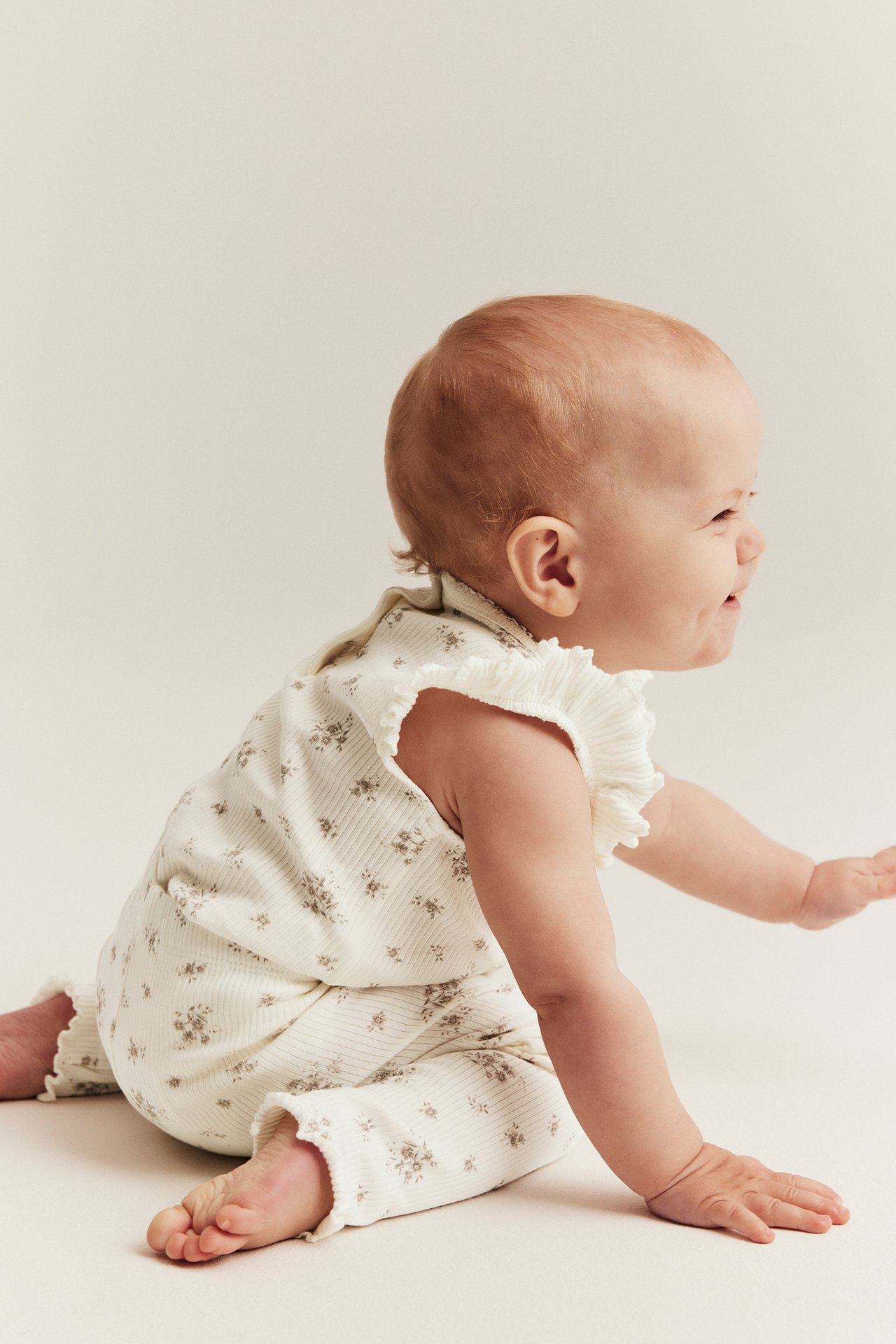 Side view of a baby wearing an off-white ribbed floral bodysuit with ruffle sleeves and matching leggings.