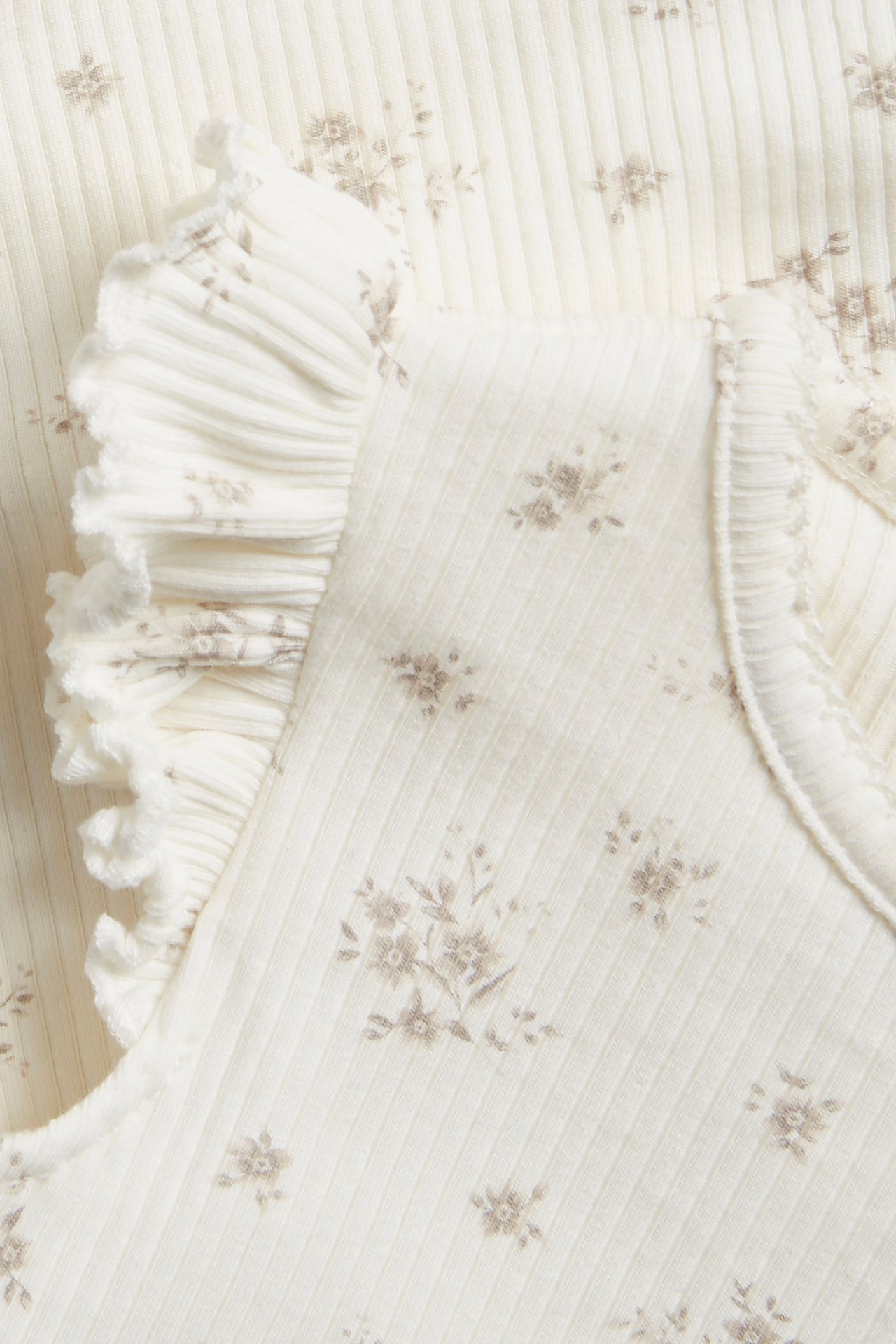 Close-up of an off-white ribbed baby body with a light floral pattern and ruffle sleeves.