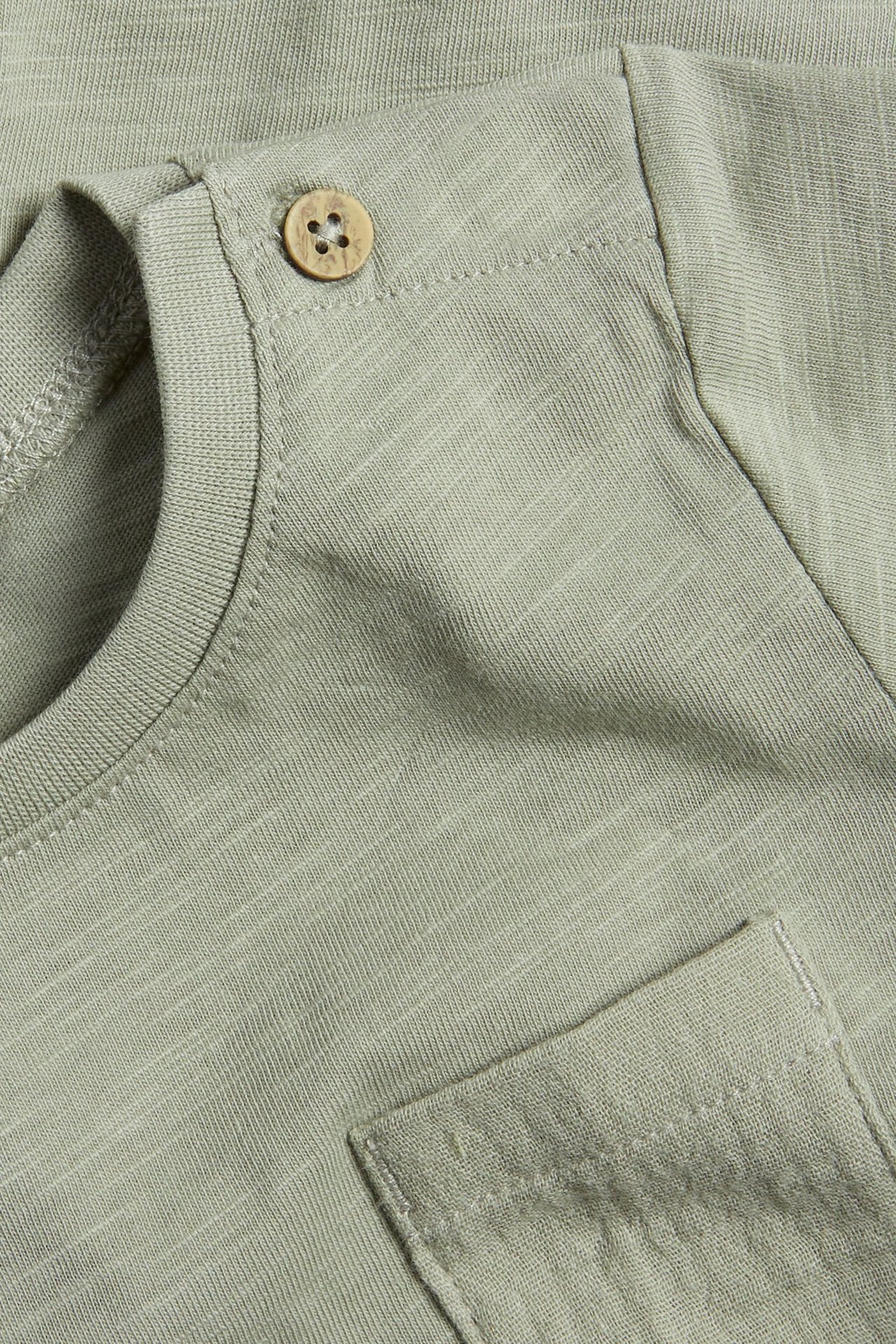 Close-up of a baby's green slub jersey short-sleeved bodysuit with a wooden shoulder button and chest pocket.