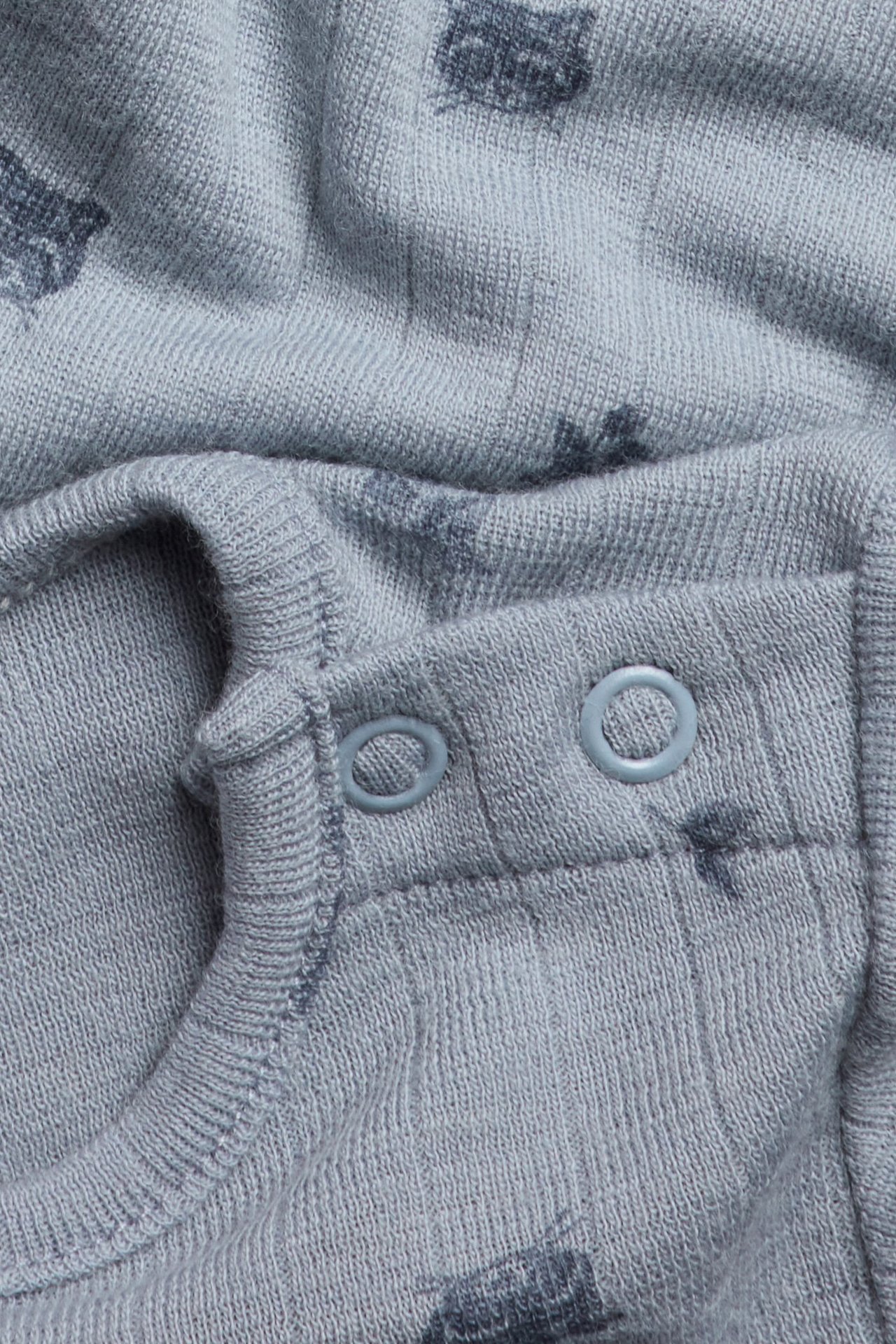 Nahaufnahme eines hellblauen gerippten Baby-Bodys aus Merinowolle mit dunklen Tiermustern und Druckknöpfen.