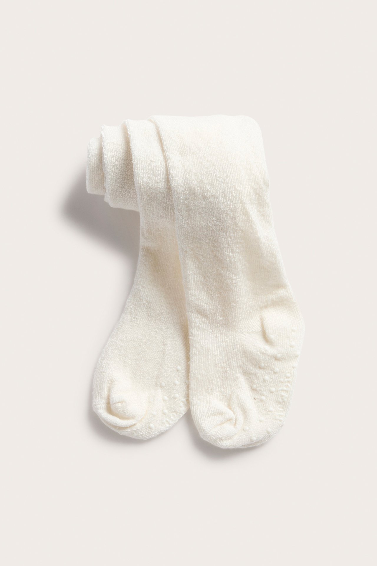 Ansicht von oben, gefaltete cremefarbene Baby-Strumpfhosen mit Anti-Rutsch-Noppen an den Sohlen.