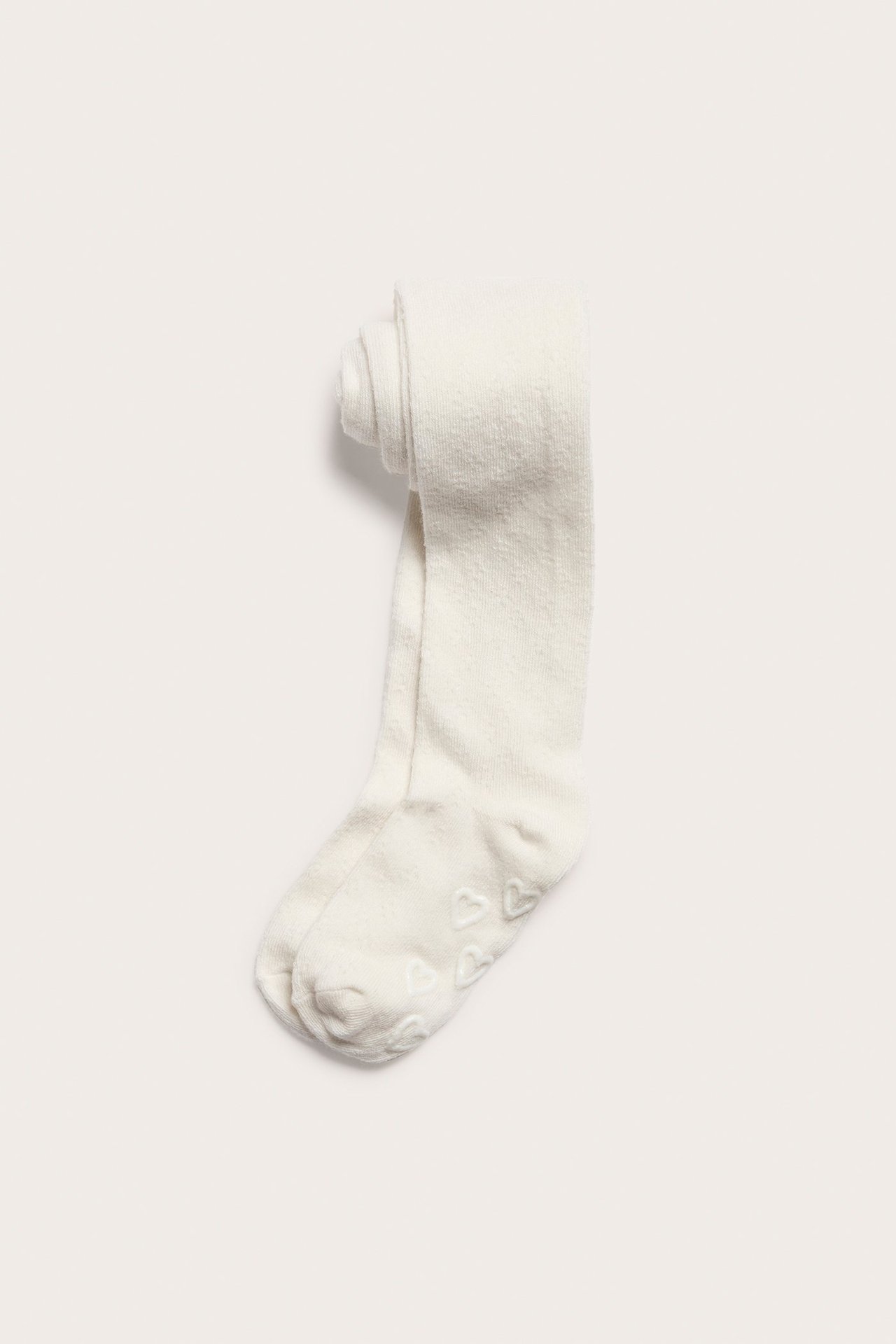 Ansicht von oben: Off-white Baby-Strumpfhose mit dezentem Lochmuster und Anti-Rutsch-Herzen an den Sohlen.