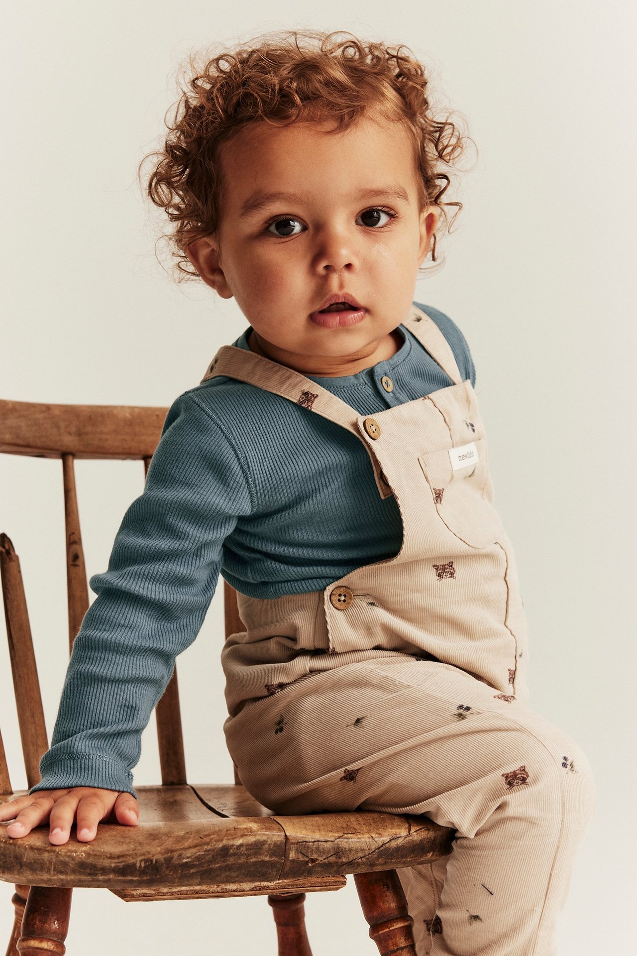 Front view of a baby wearing a blue ribbed long-sleeved bodysuit under beige corduroy dungarees with a small animal print.