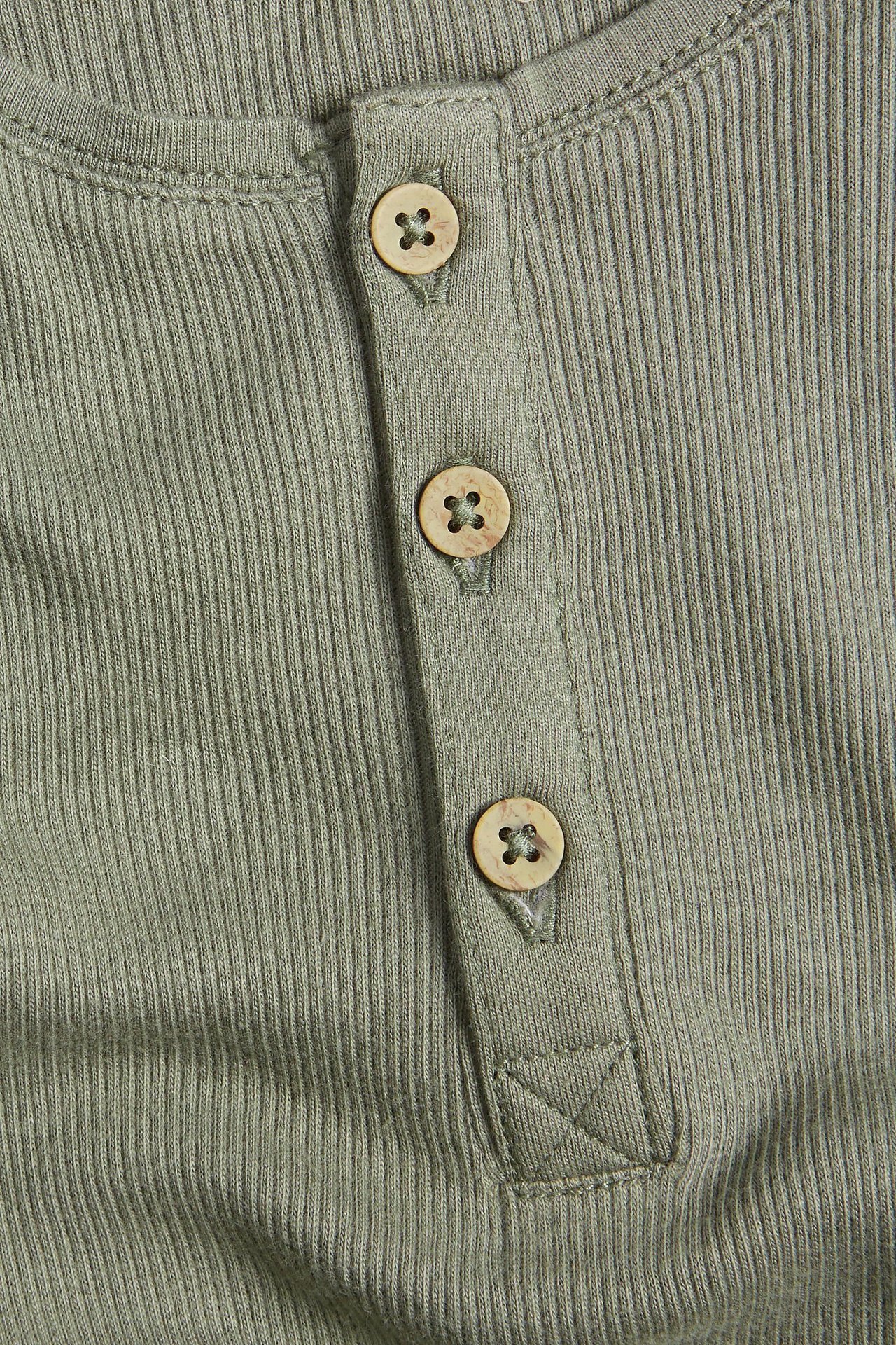 Nahaufnahme eines grünen gerippten Baby-Bodys aus Baumwolle mit Dreiknopfleiste.