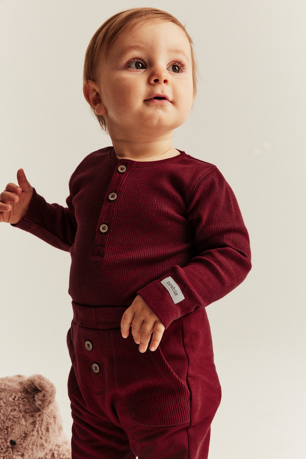 Baby in roter, ribsümmiger Langarm-Body mit Knopfleiste vorne und Druckknöpfen im Schritt.