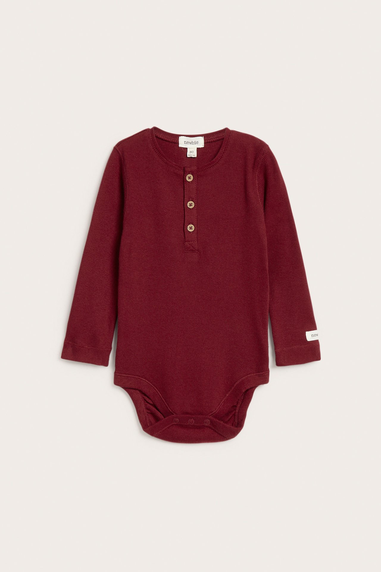 Vorderansicht eines weinroten Baby-Bodys aus Rippstrick-Baumwolle, mit Knopfleiste und Druckknöpfen im Schritt.