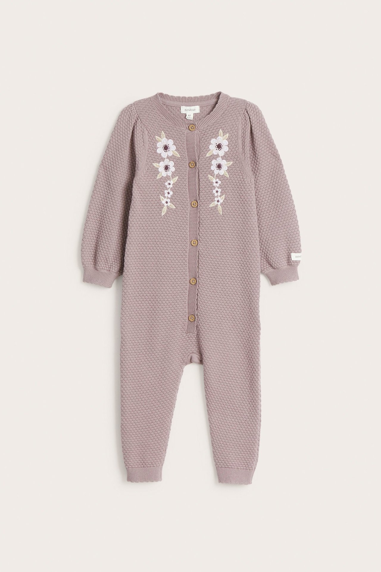 Vorderansicht eines babyhelllila strukturstrick-Baumwollstramplers mit Blumenstickerei und Knöpfen vorne.