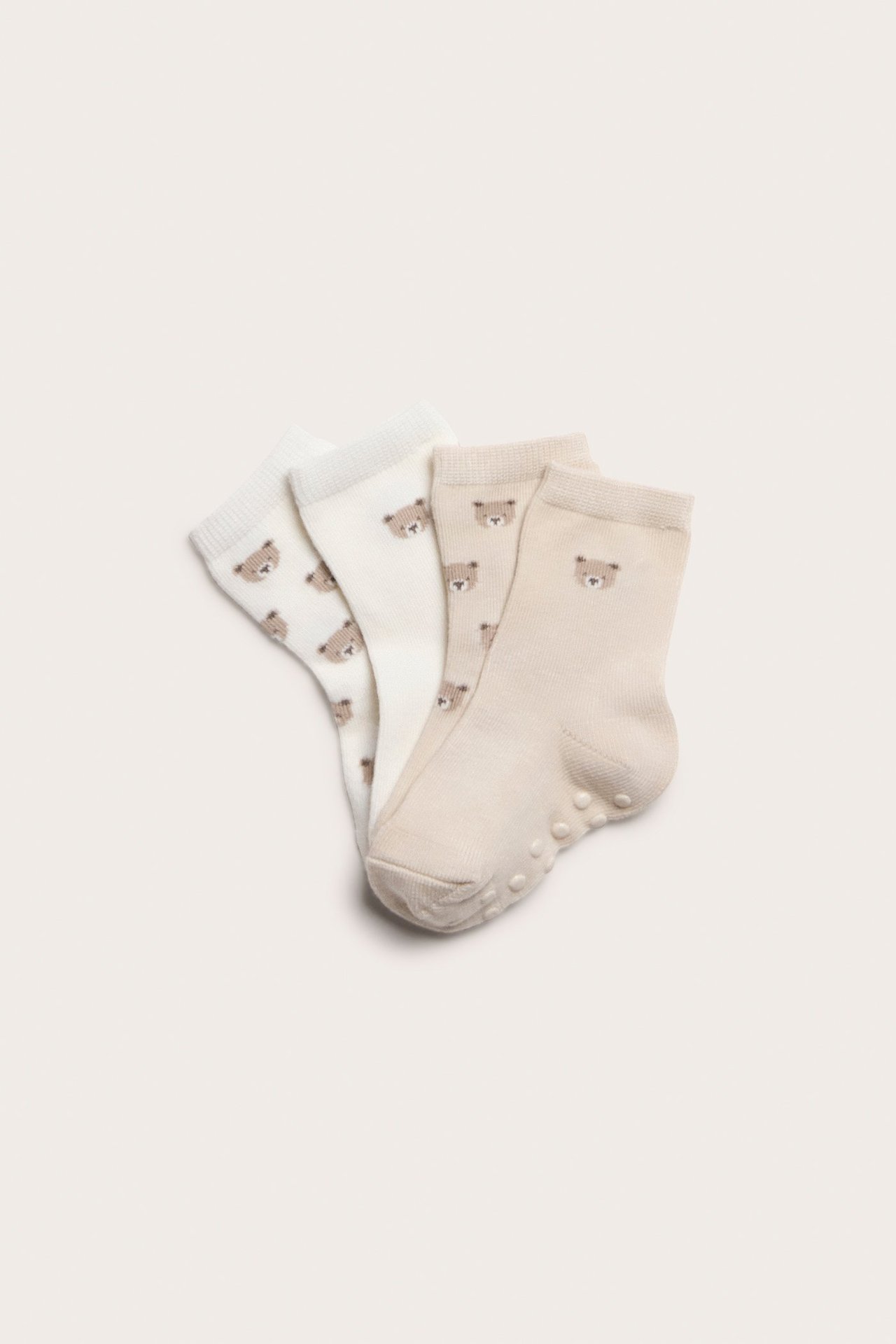 Draufsicht: Vier Paar Babysocken, hellbeige und cremeweiß, mit Bärenmustern und Antirutsch-Noppen.