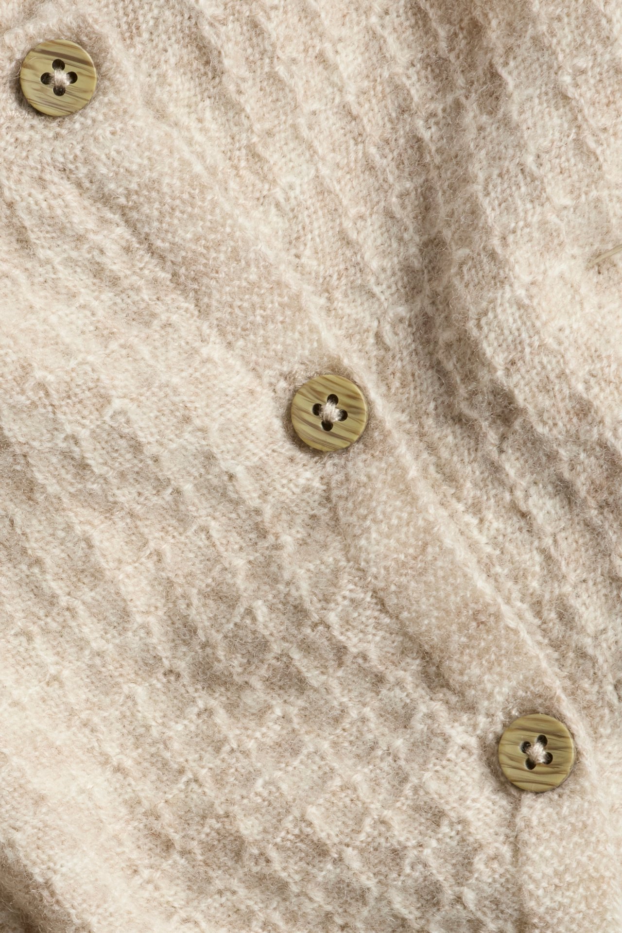 Close-up of a beige melange textured knit wool and cashmere blend cardigan with green buttons.
