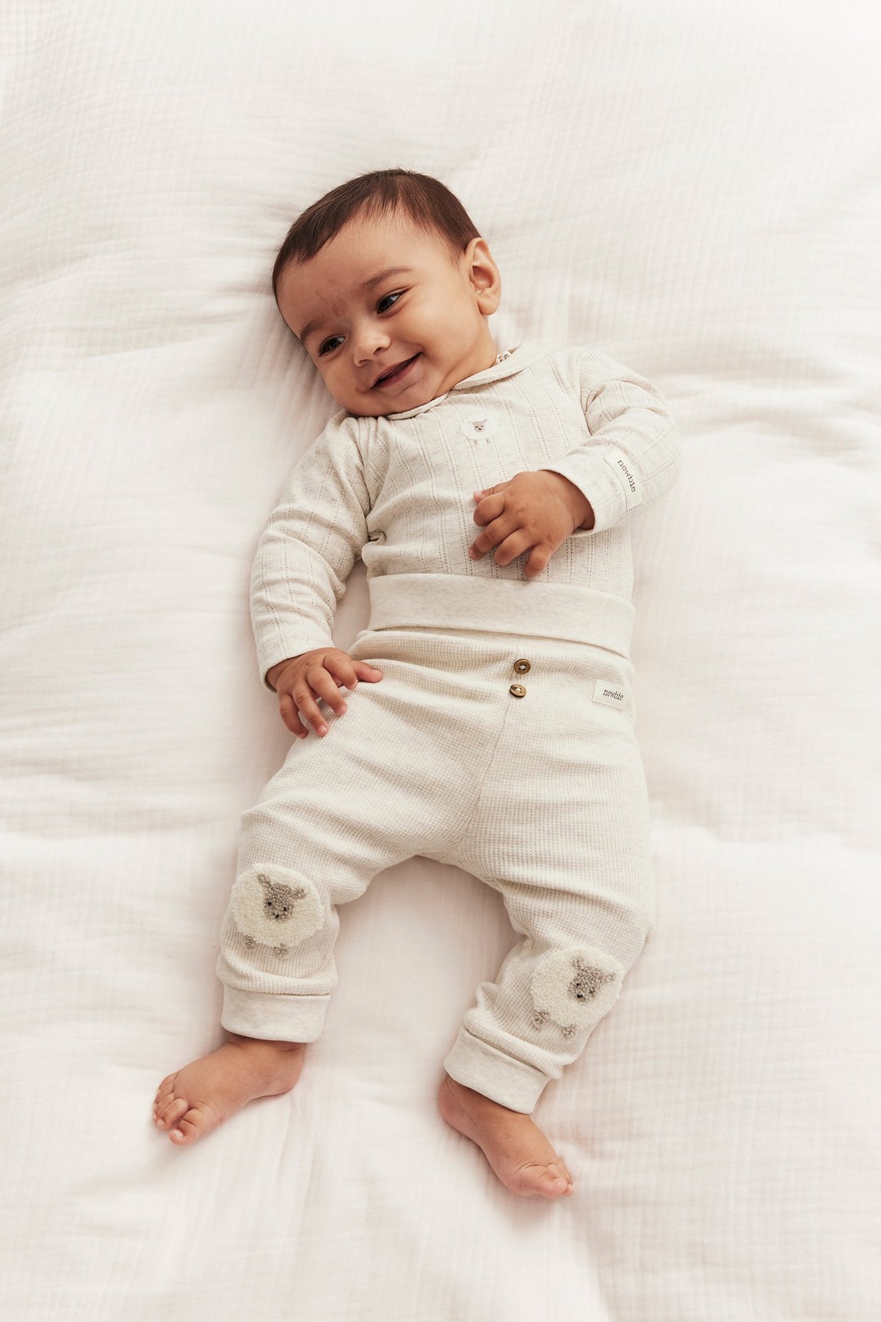 Baby in a beige melange ribbed long-sleeved body with collar, chest embroidery, and matching trousers with sheep appliques.