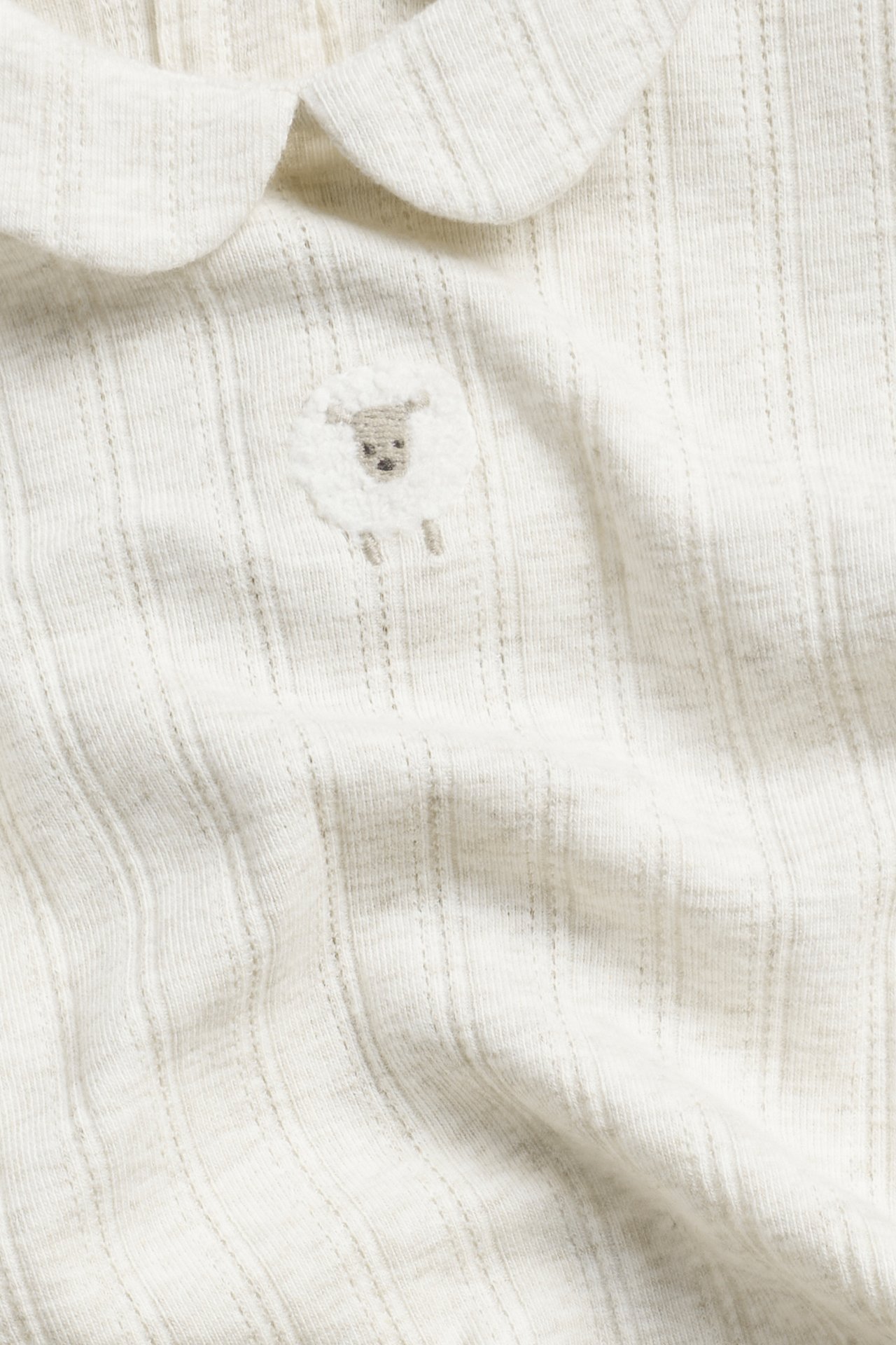 Nahaufnahme eines beigefarbenen melierten gerippten Baby-Bodys mit Rundkragen und Schafstickerei.