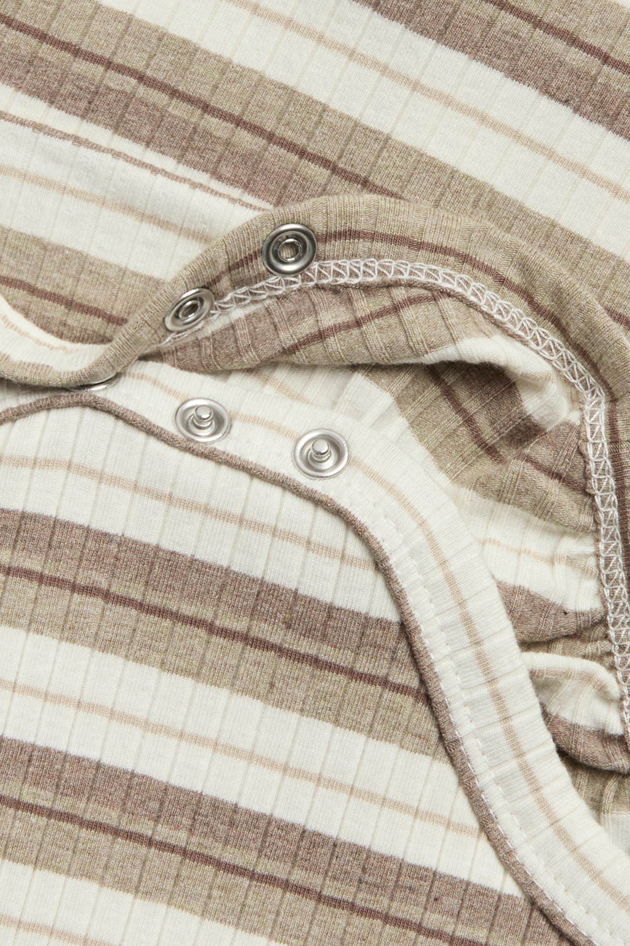 Nahaufnahme eines beige-weiß gestreiften gerippten Babybodys mit silbernen Druckknöpfen.