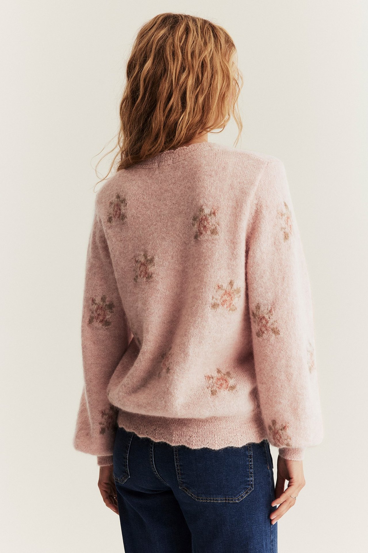 Rückenansicht einer Frau in rosa Mohair-Strickpullover mit Jacquard-Rosenmuster und dunkelblauen Jeans.